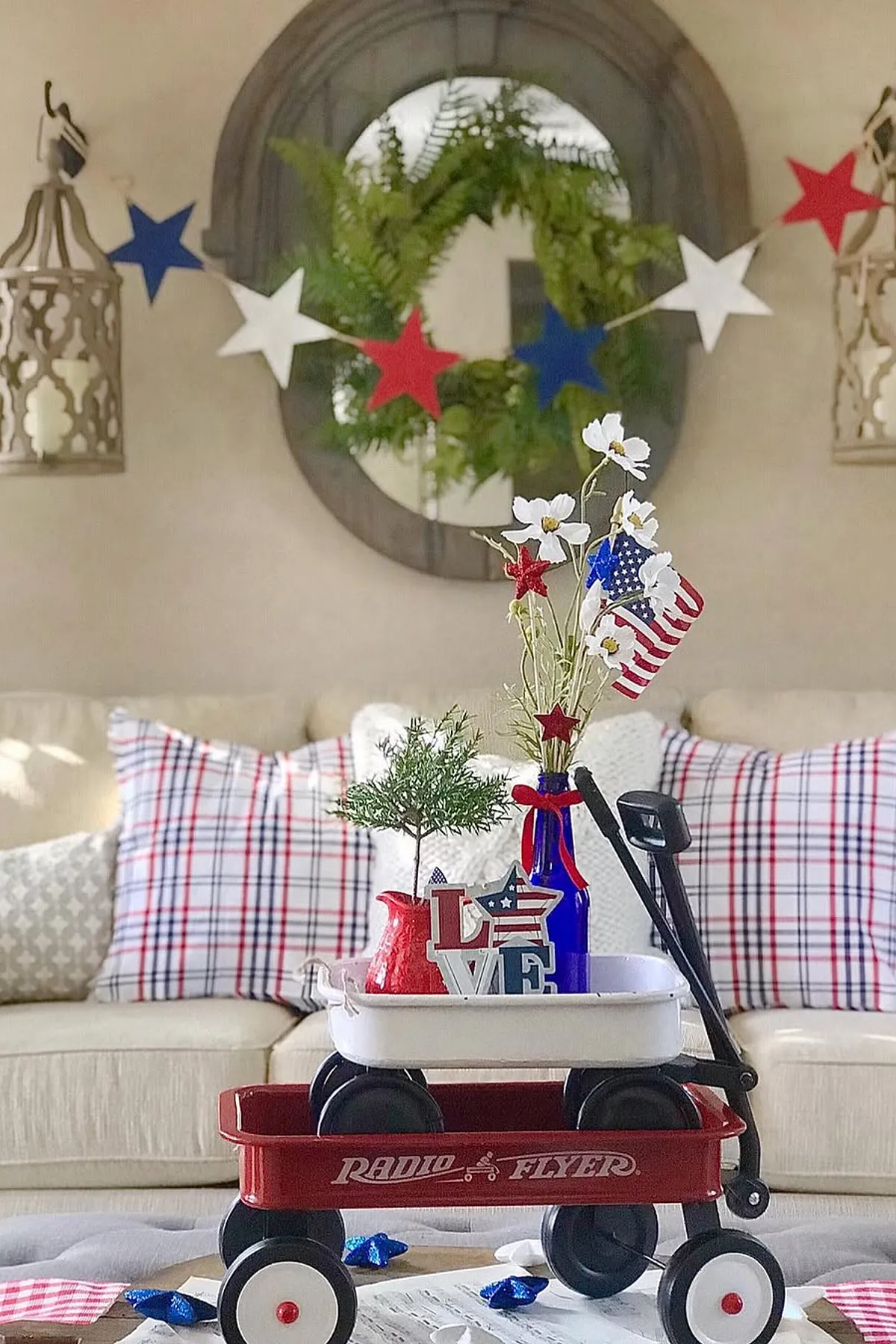 A red wagon filled with patriotic decor, including flowers and stars, against a cozy living room backdrop.
