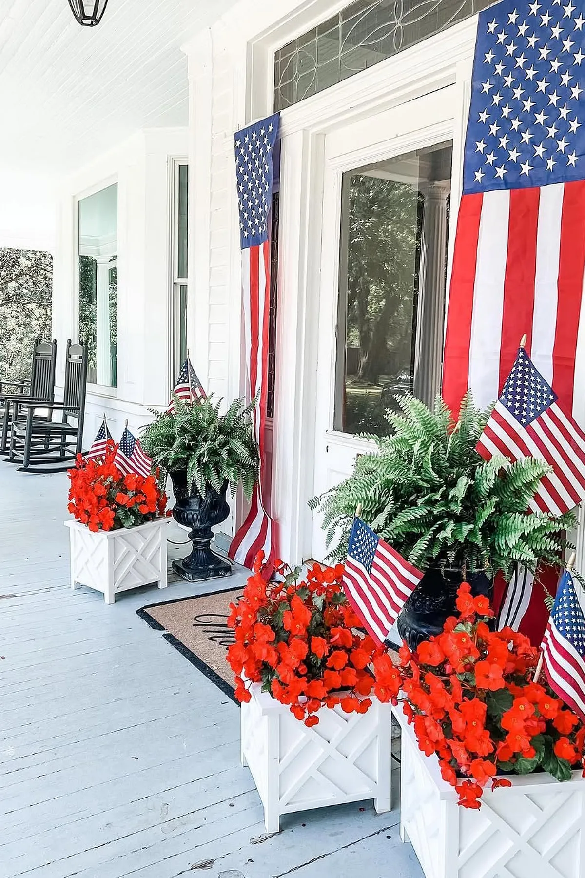 A charming porch adorned with American flags, vibrant red flowers in planters, and classic rocking chairs.