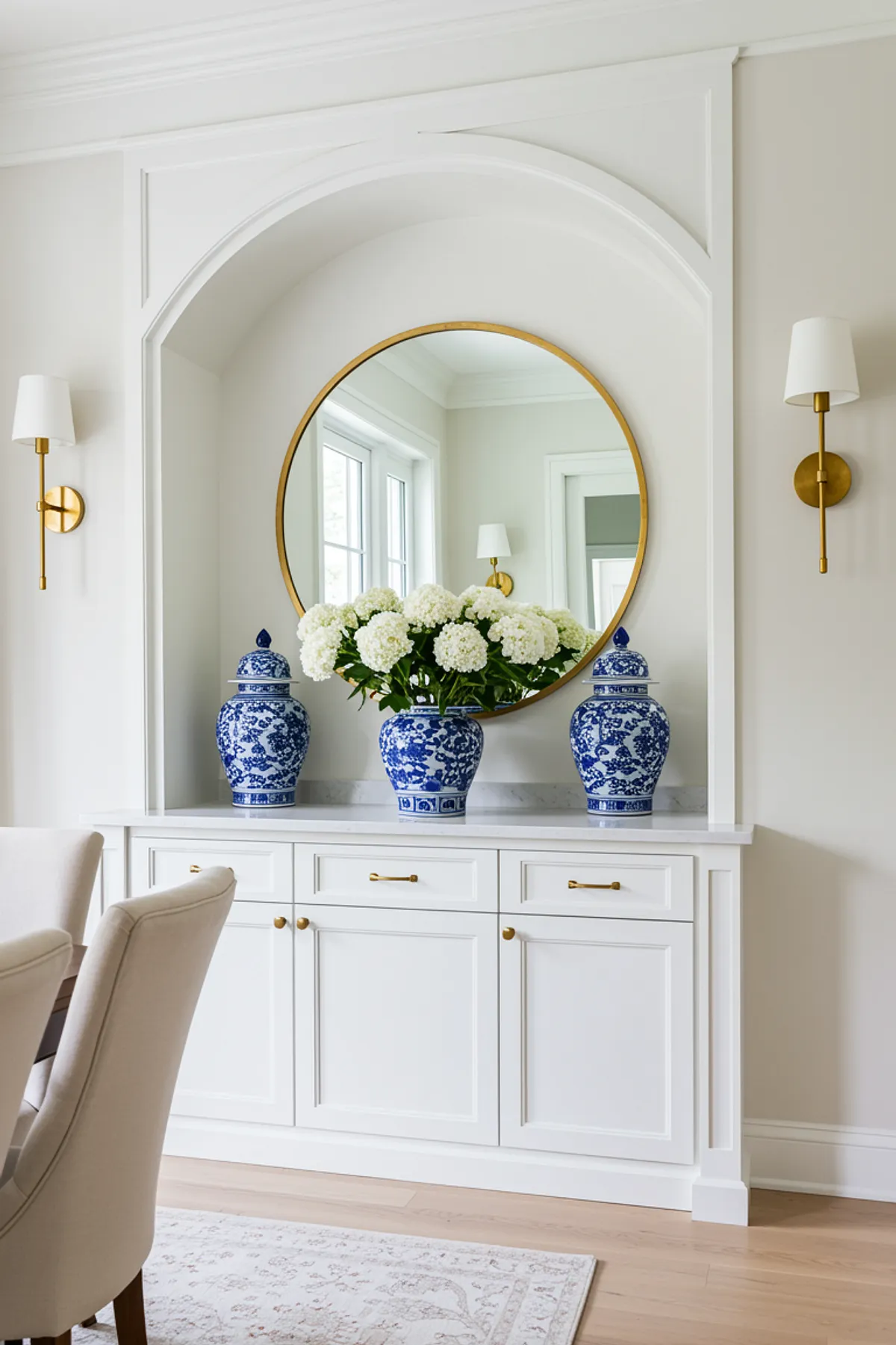 Elegant dining room featuring white built-in cabinets, blue porcelain vases, round mirror, and fresh hydrangeas.