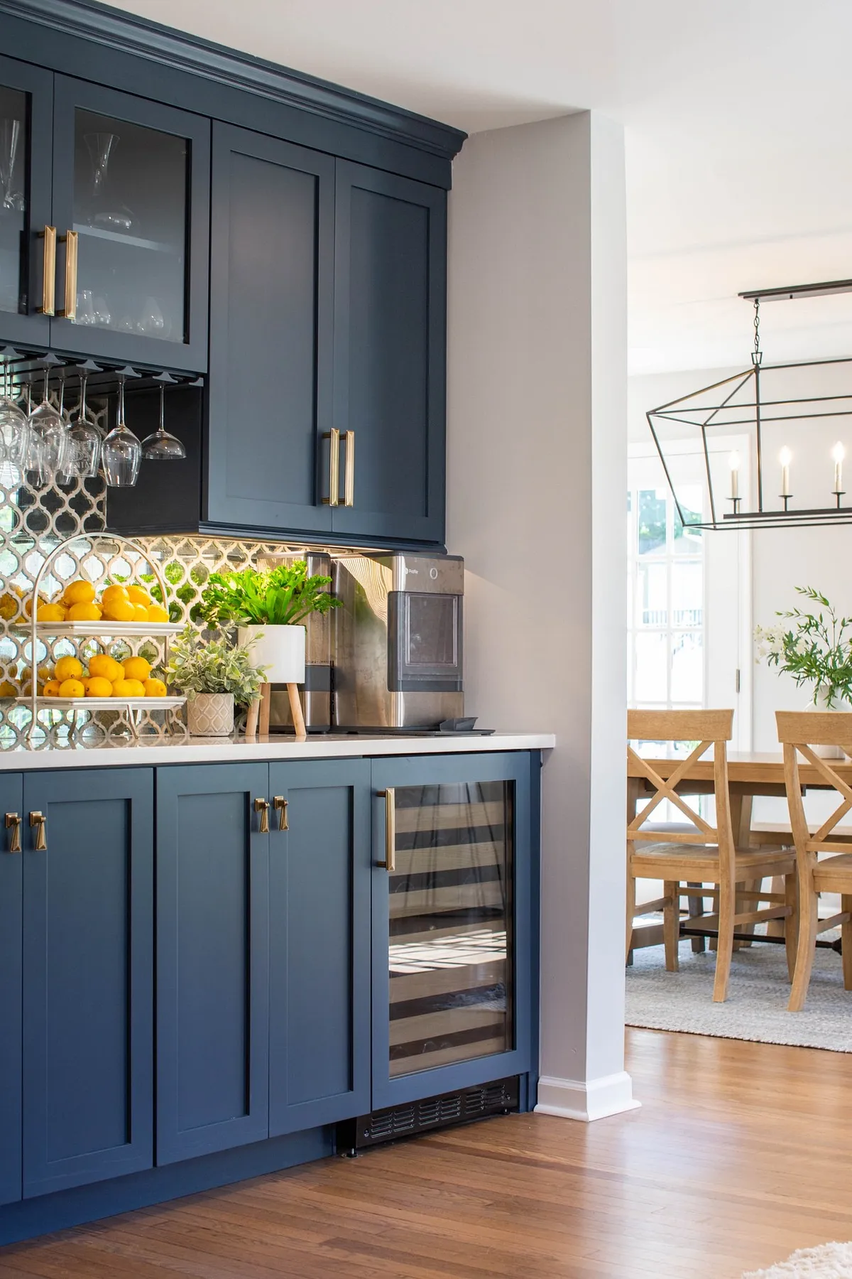 Modern dining room featuring navy built-in cabinets, glass shelving for display, wine cooler, and decorative citrus fruits.