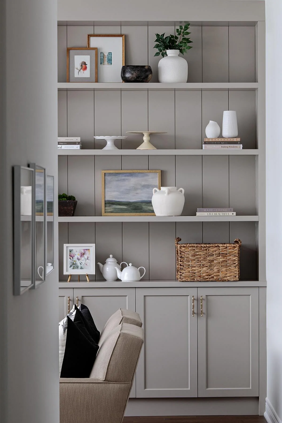 Modern dining room featuring light gray built-in cabinets, decorative shelves with vases and artwork, and practical storage.