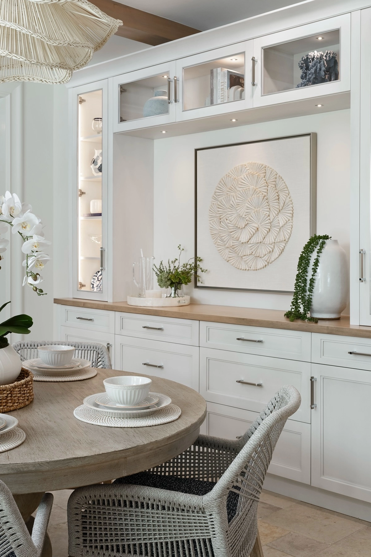 Chic dining room featuring white built-in cabinets, round wooden table, wicker pendant light, and decorative accents.
