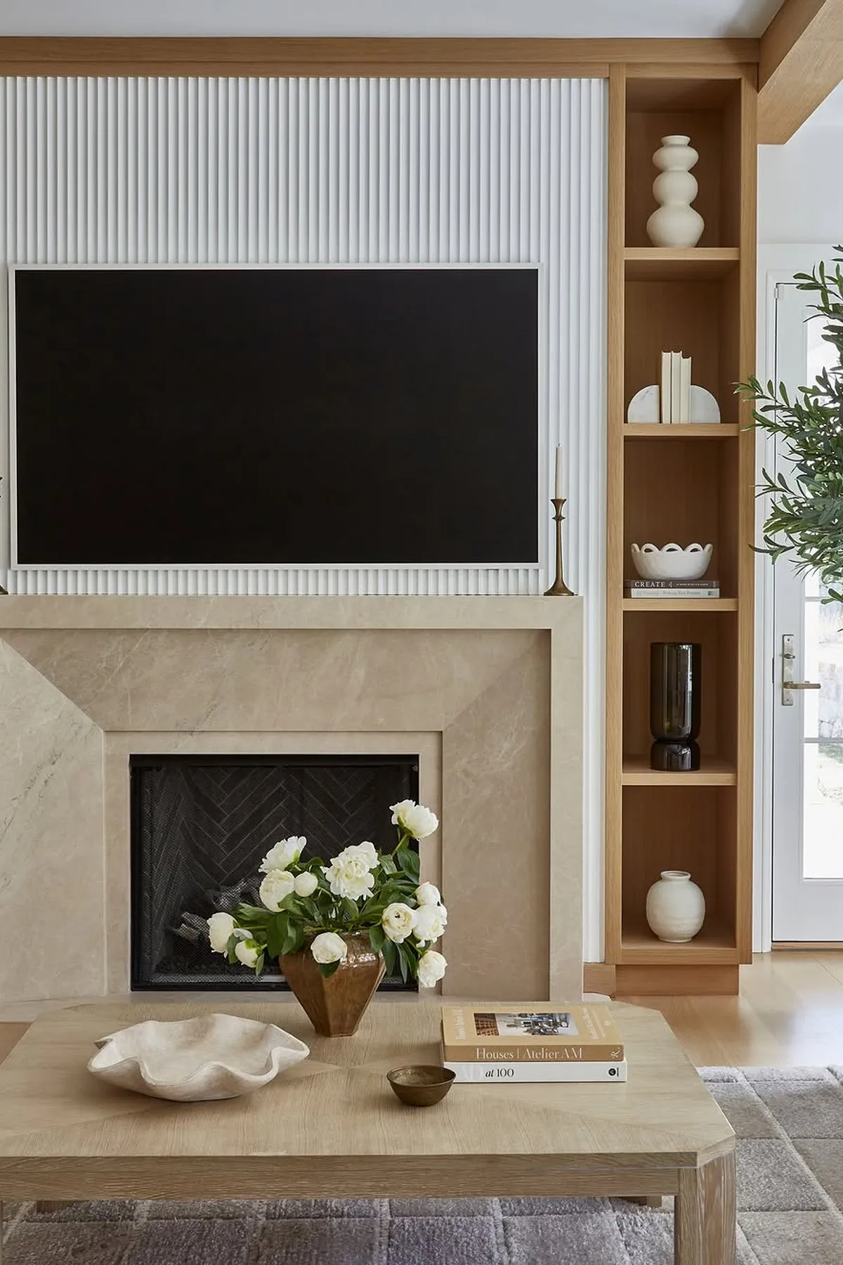 Modern living room with sleek TV wall featuring white paneling, marble fireplace, decorative shelves, and cozy accents.