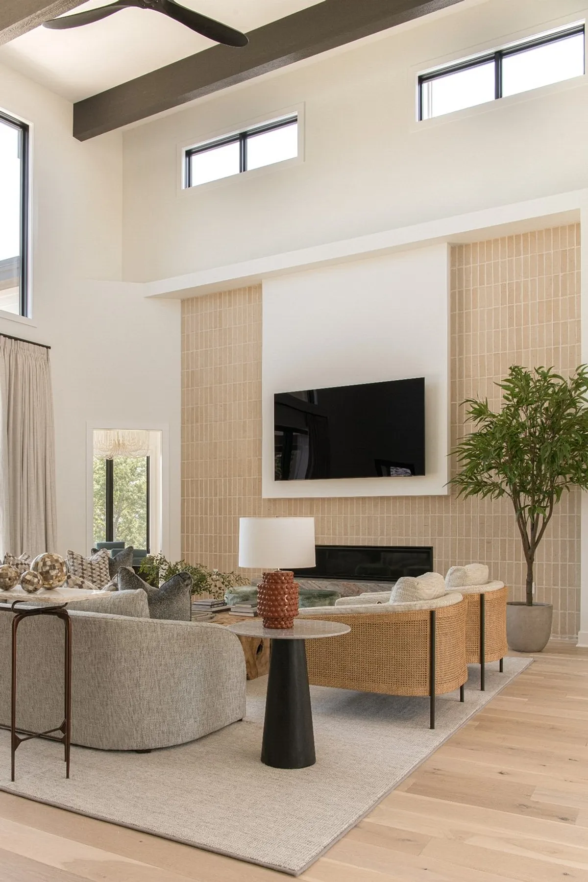 Modern living room featuring a stylish TV wall with beige tiles, sleek TV, natural decor, and cozy seating.