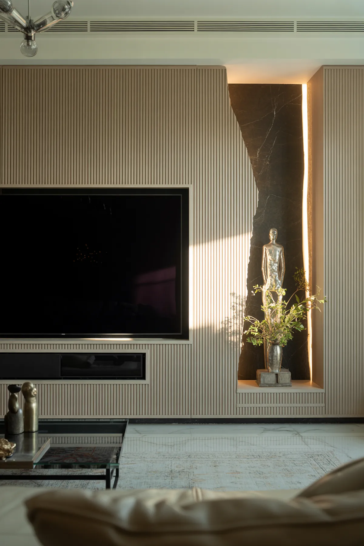 Modern TV wall featuring textured paneling, sleek TV, sculptural decor, and soft lighting in a stylish living room.