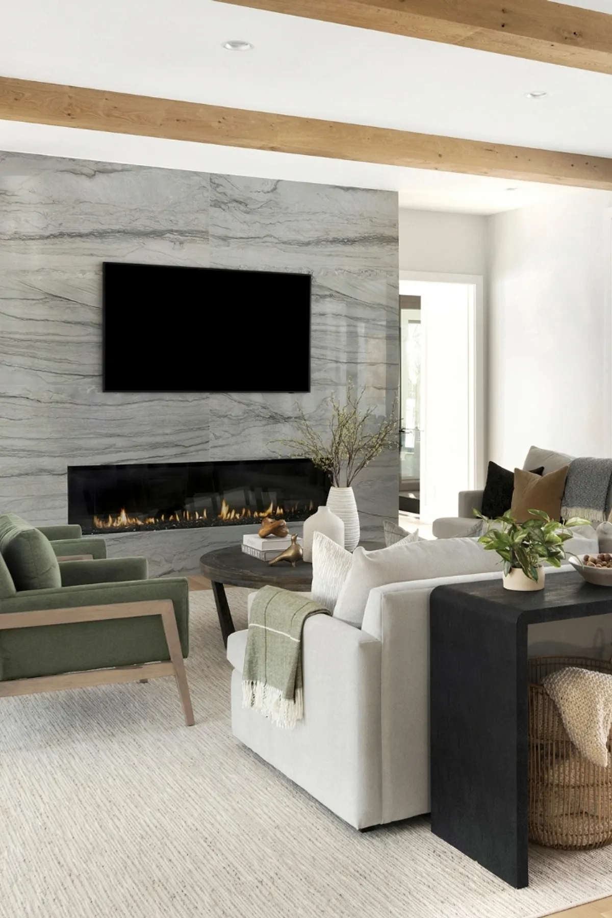 Stylish living room with a marble TV wall, cozy green chairs, modern fireplace, and elegant decor.