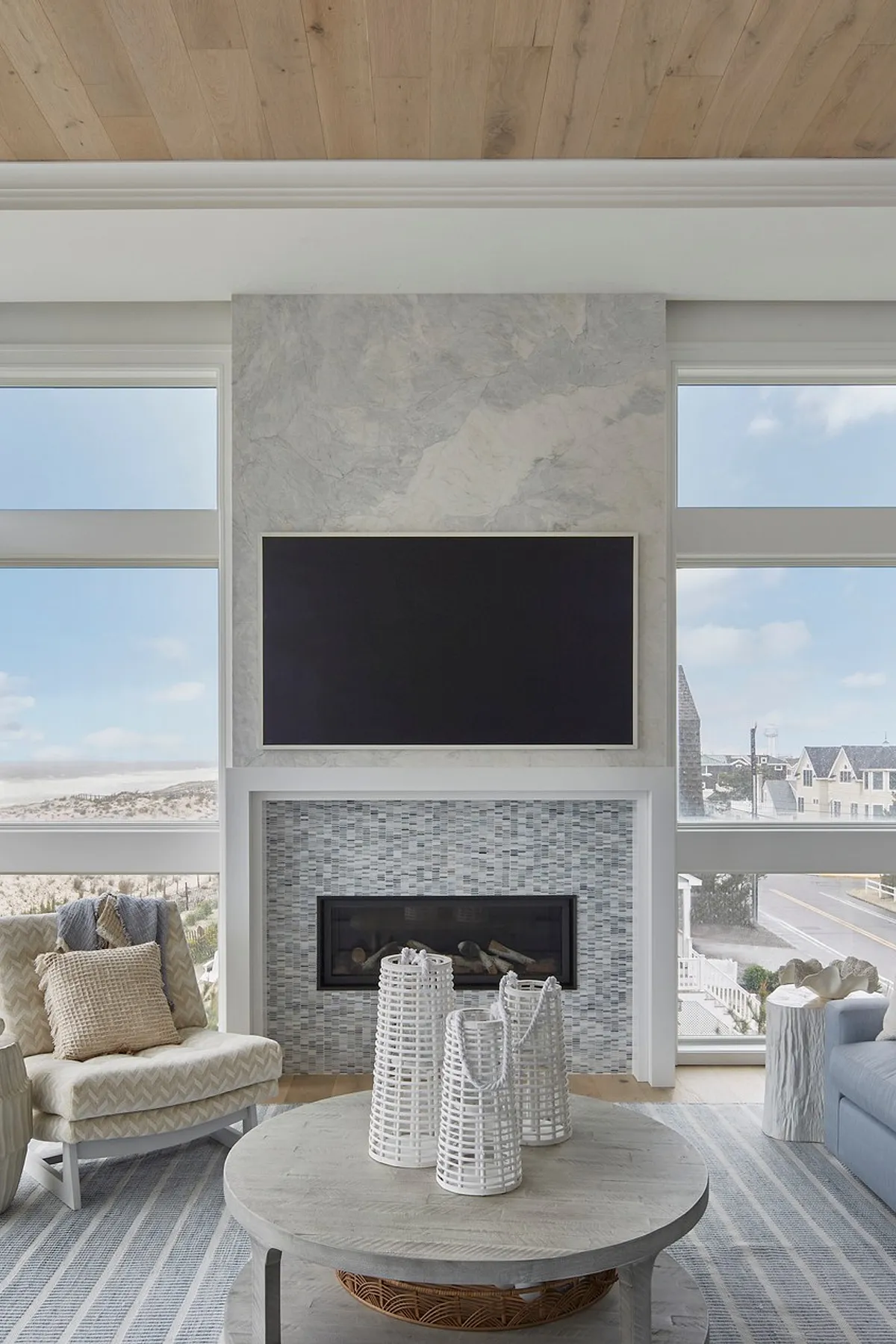 Modern living room featuring a marble TV wall, cozy furniture arrangement, and natural light from large windows.