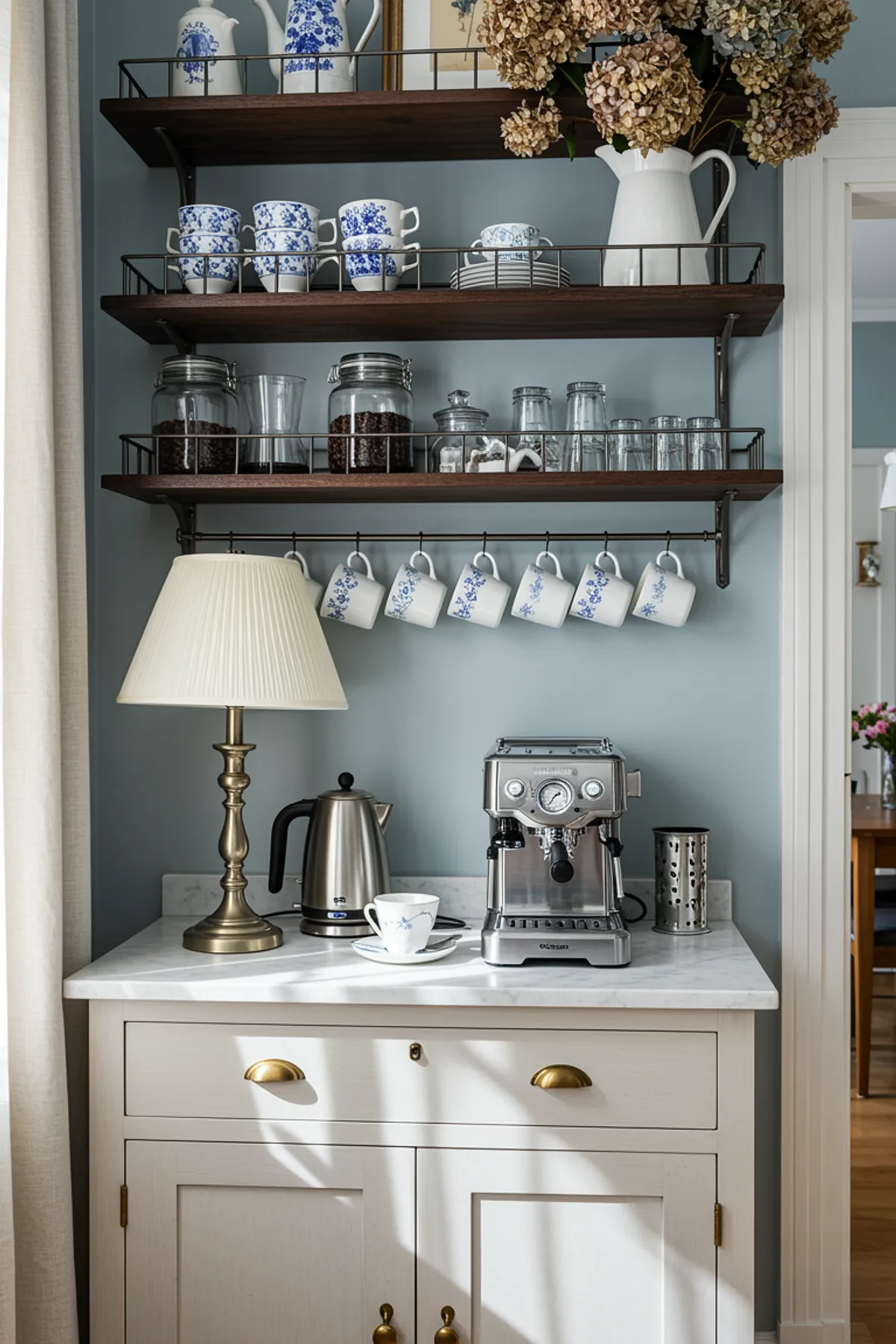 Coffee station with dark wood shelves, blue and white mugs on metal racks, glass jars, espresso machine, and table lamp.