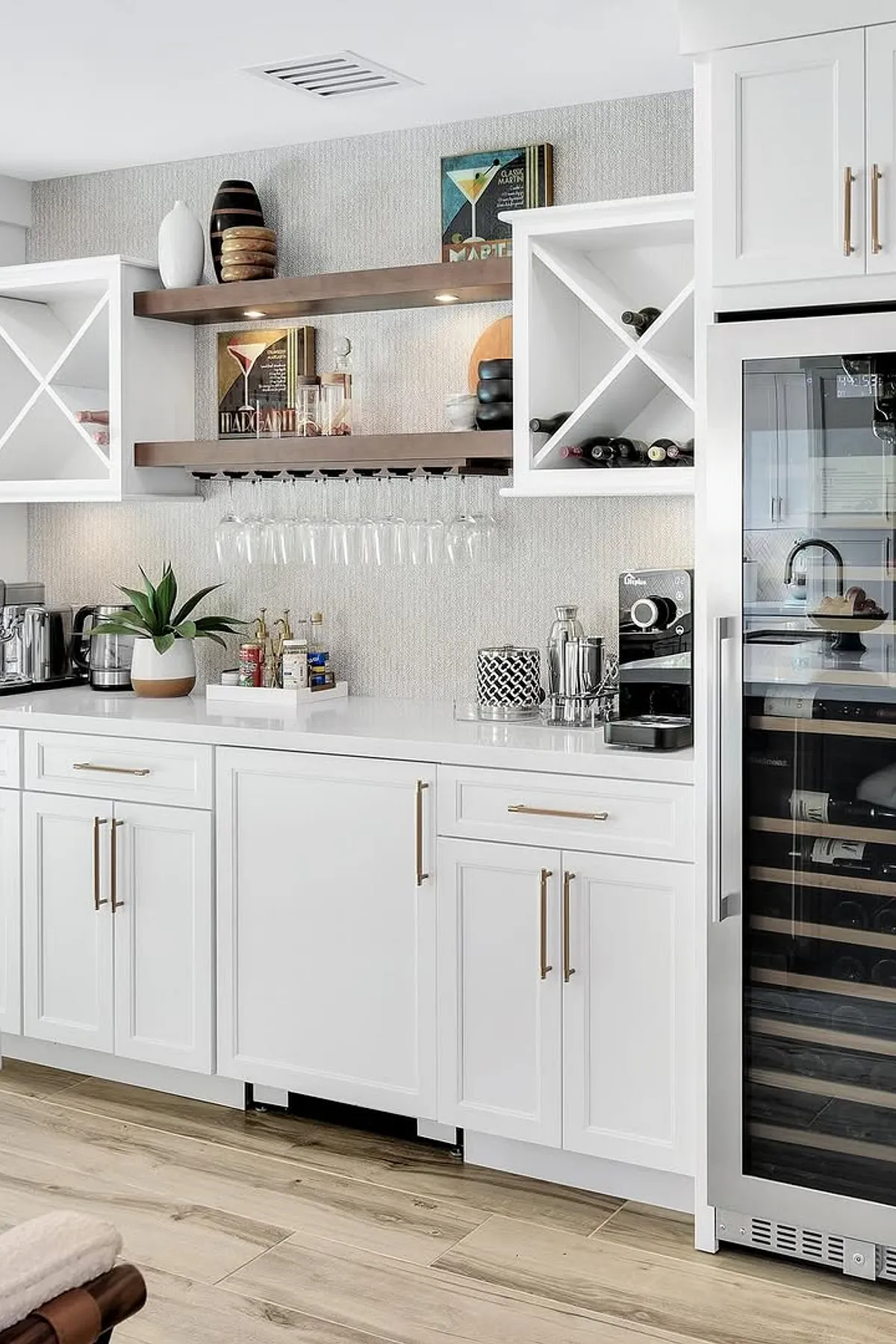 White cabinets with brass handles, built-in wine storage, glassware shelf, and a coffee machine on the countertop.