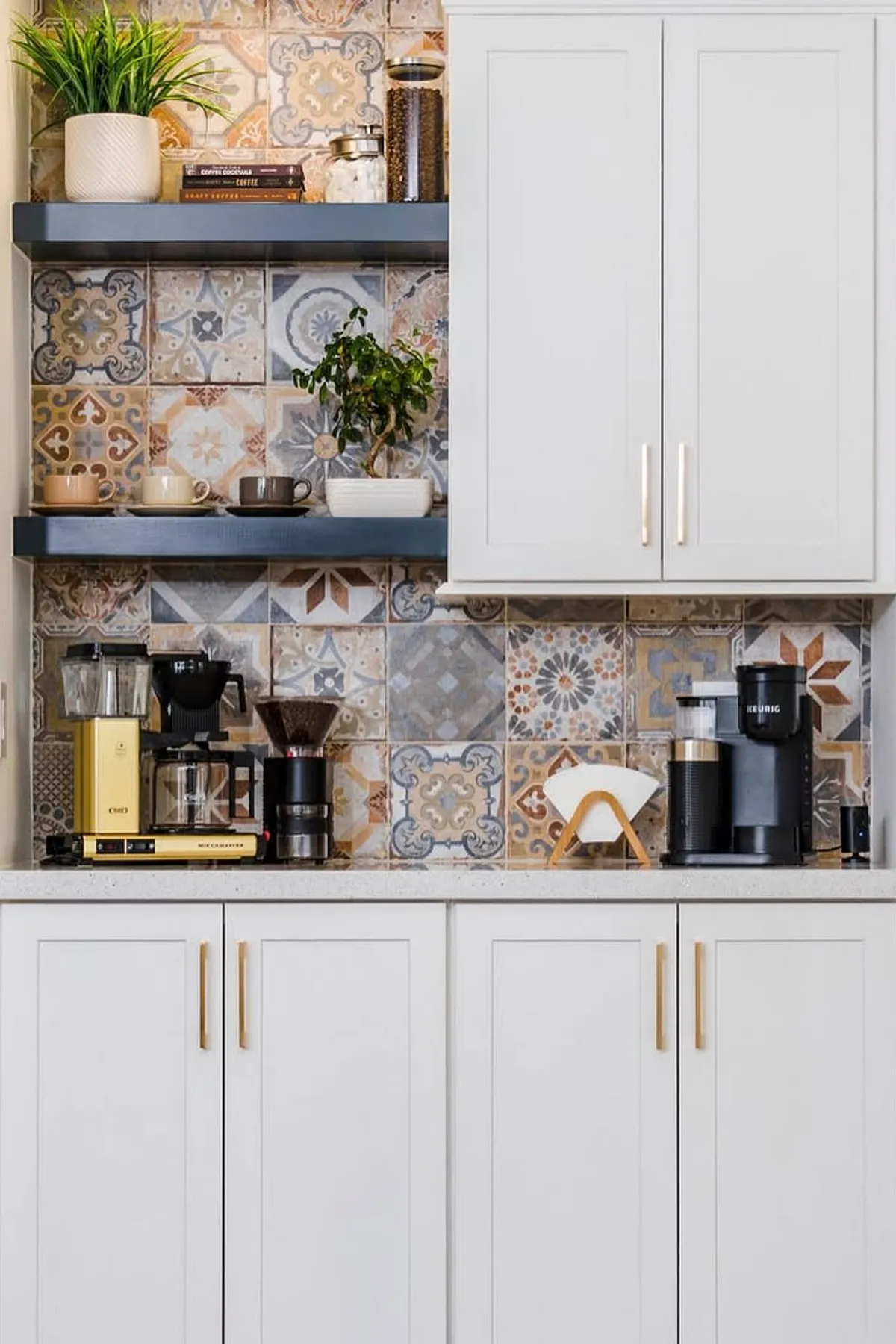 Coffee station with patterned tile background, black shelves, and white cabinets with brass handles.