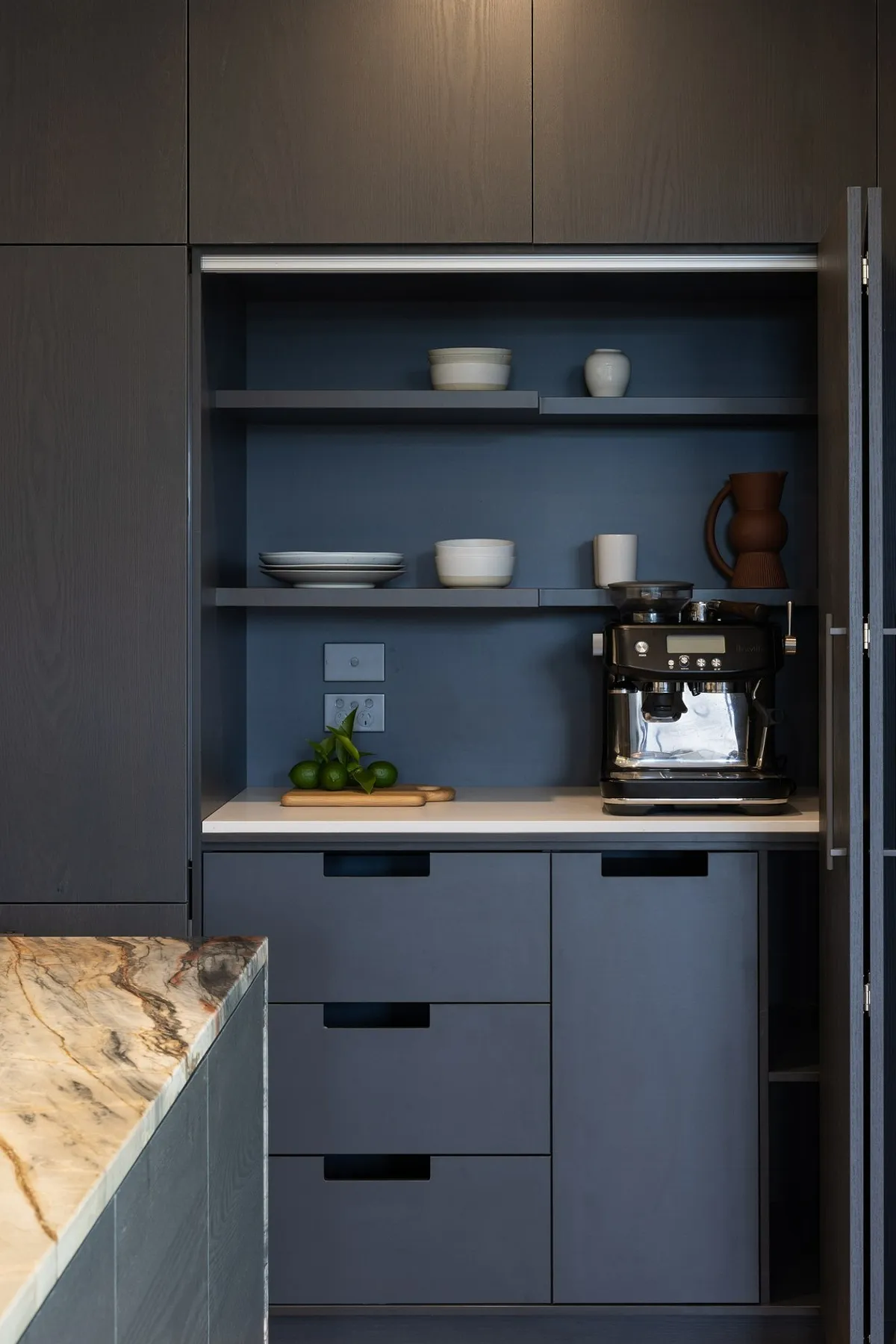 Dark wood cabinets with open shelving holding white dishes, espresso machine, and limes on the counter.