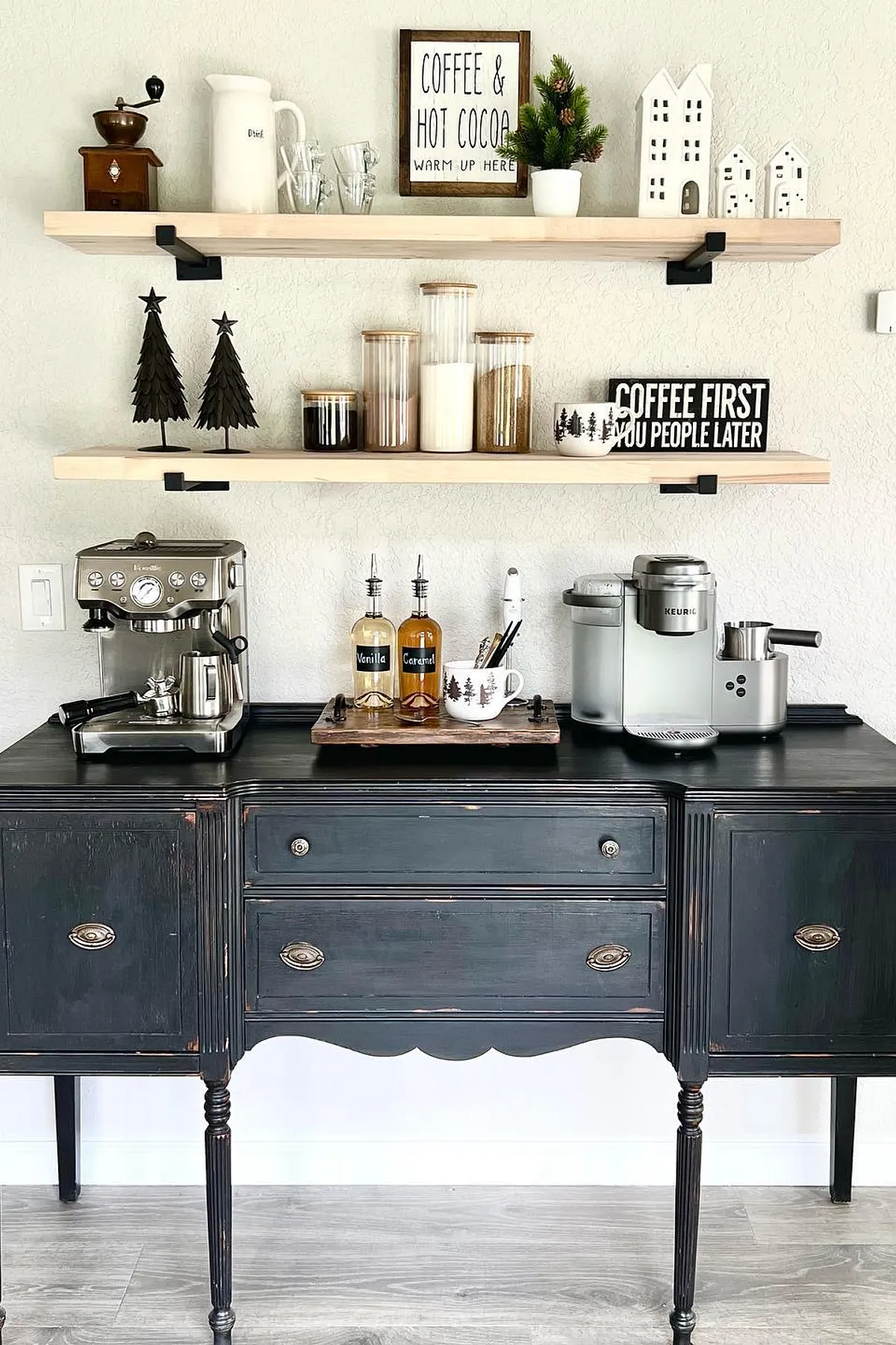 Black vintage buffet with coffee machines on top and decorative shelves above featuring jars and signs.