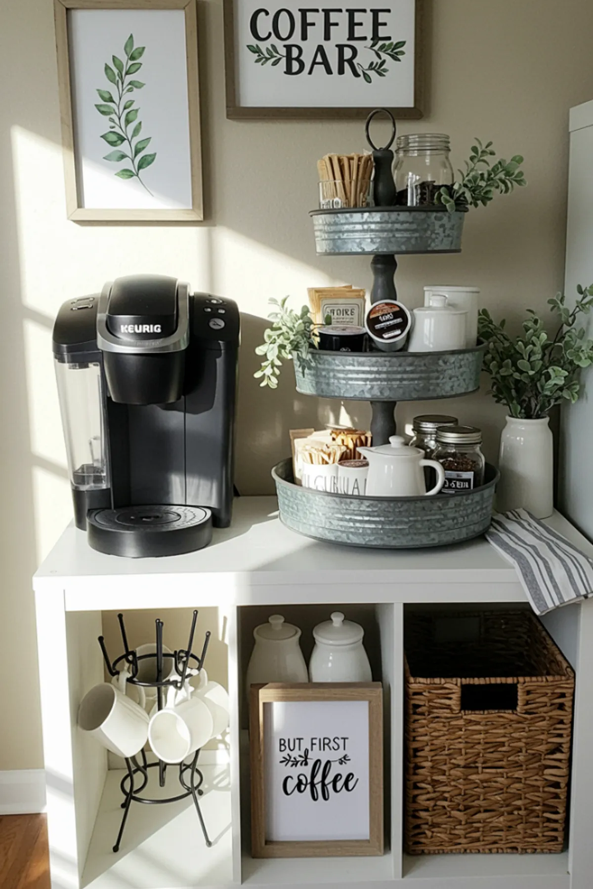 Coffee station with tiered trays holding mugs and accessories, framed signs, and a Keurig machine on a white cabinet.