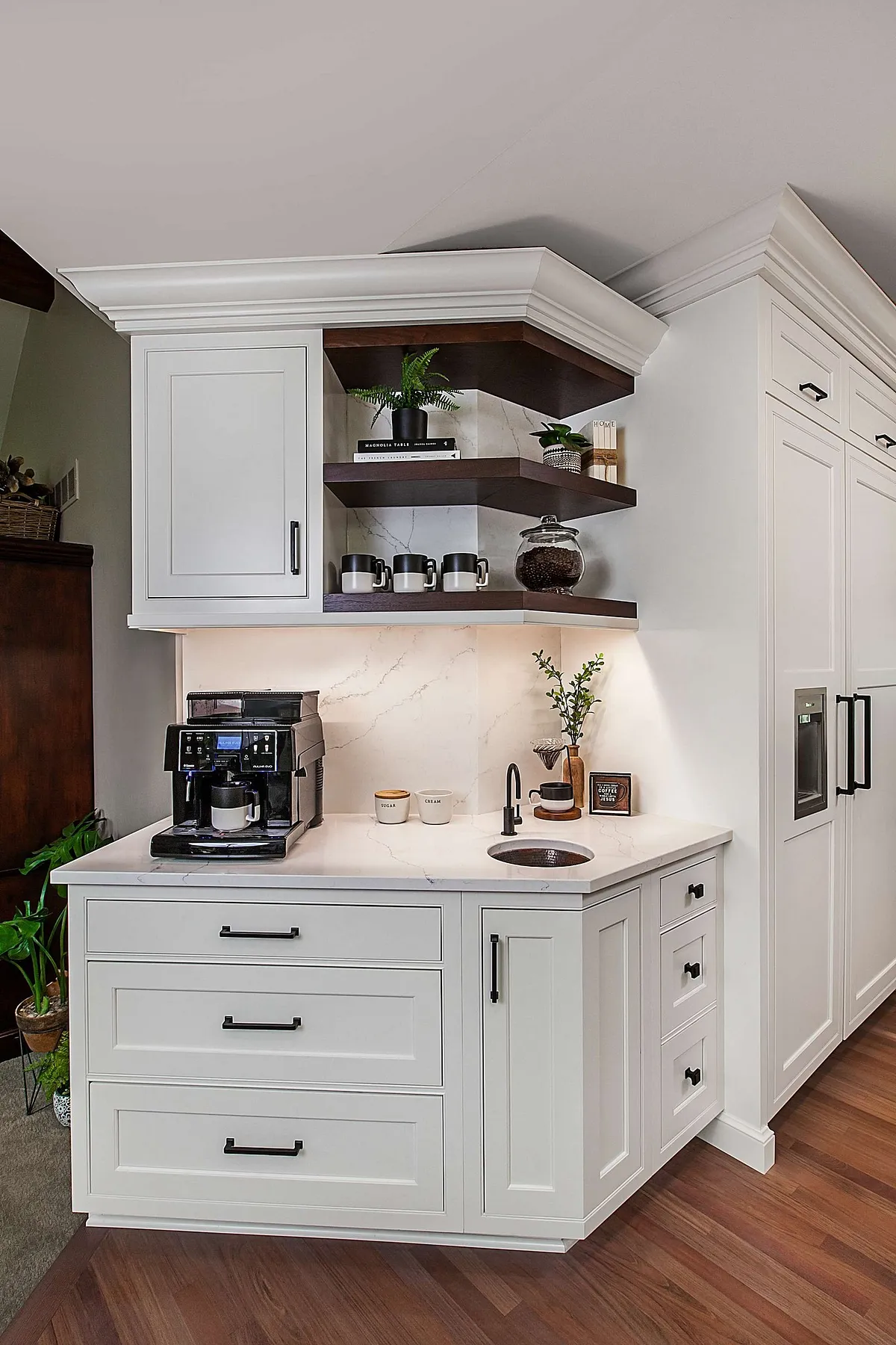 White coffee station with dark wood shelves, espresso machine, and small sink.