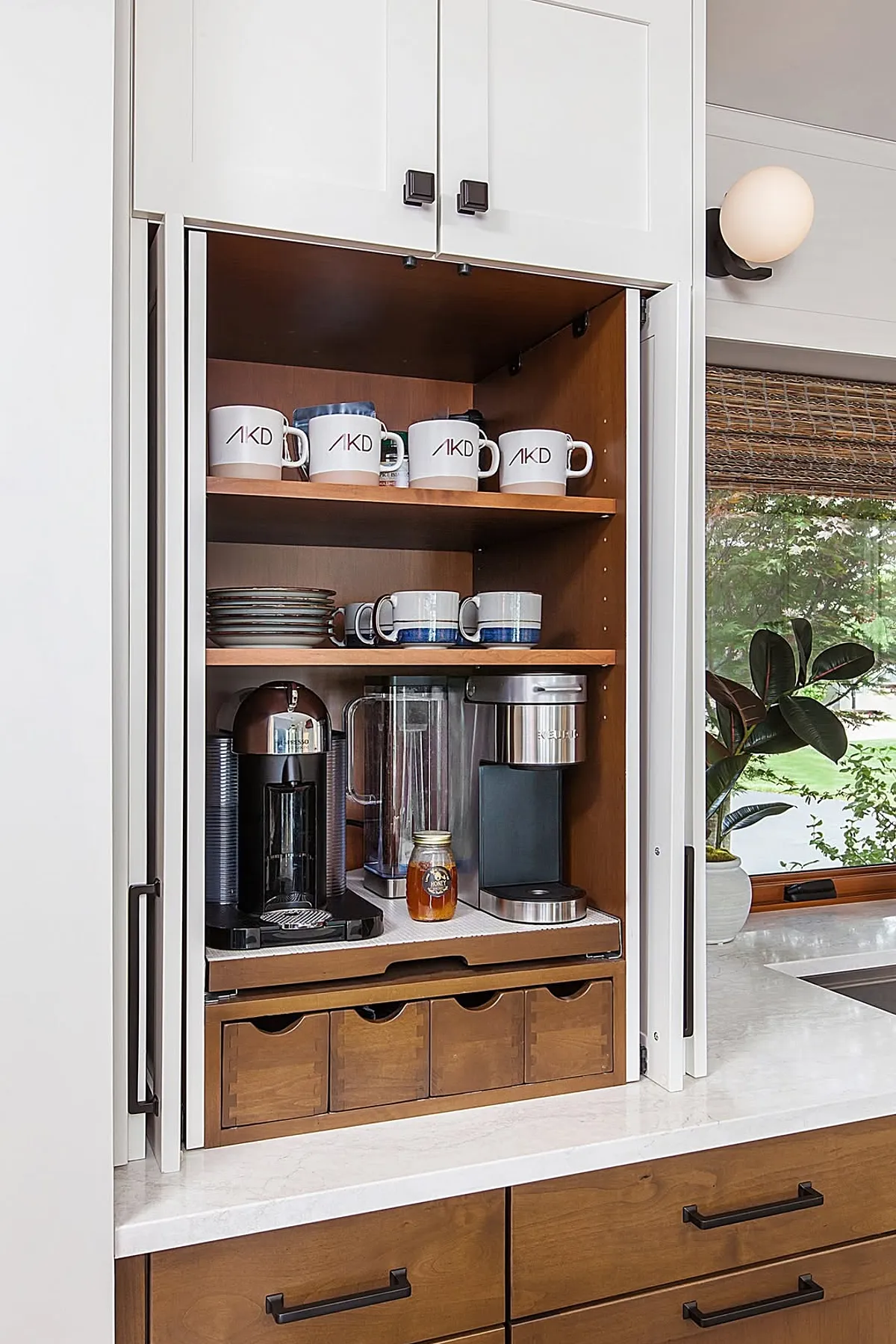Wooden interior cabinet coffee station with mugs and appliances inside white cabinetry.