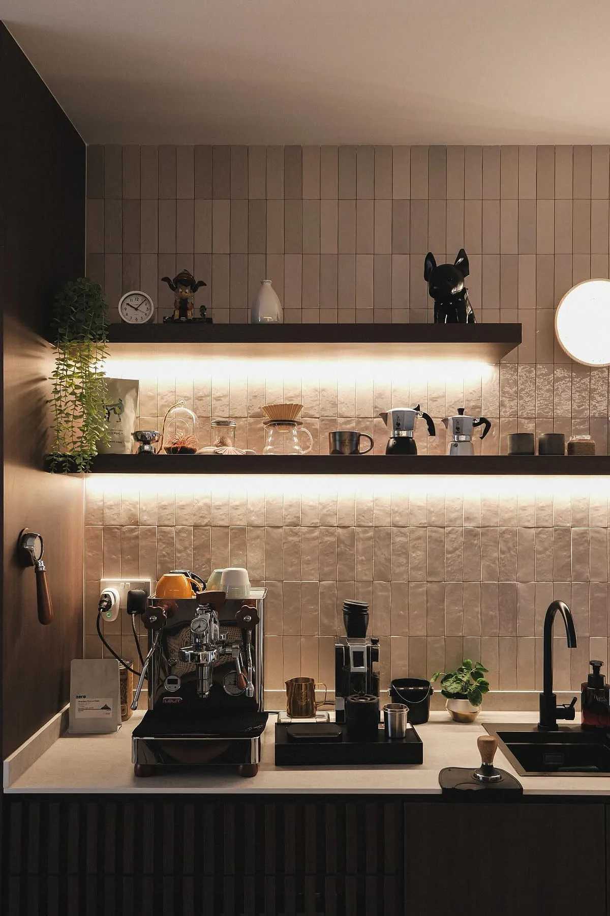 Coffee station featuring espresso machine, dark wooden shelves with LED lighting, and textured wall tiles.