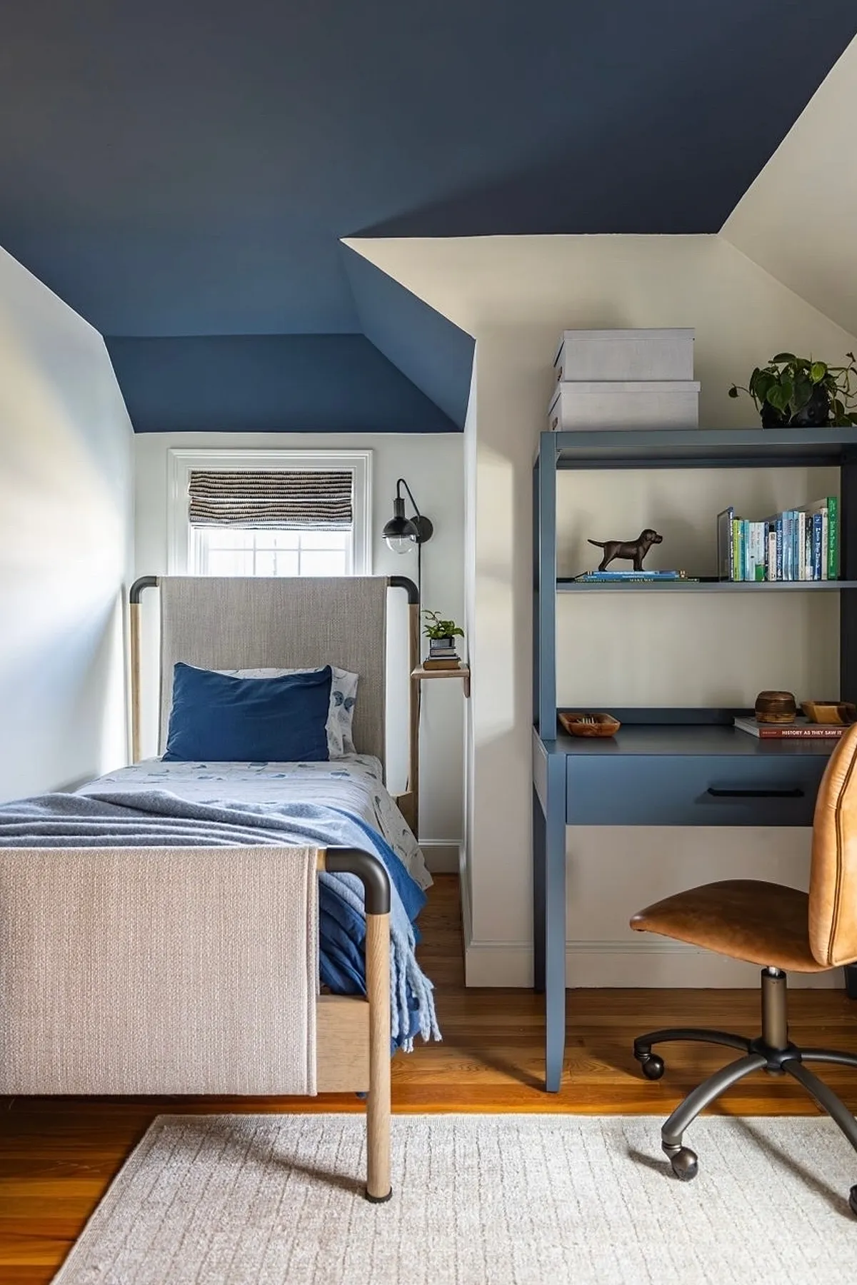 Bedroom with navy ceiling, blue accent desk, single bed with blue bedding, and white walls.