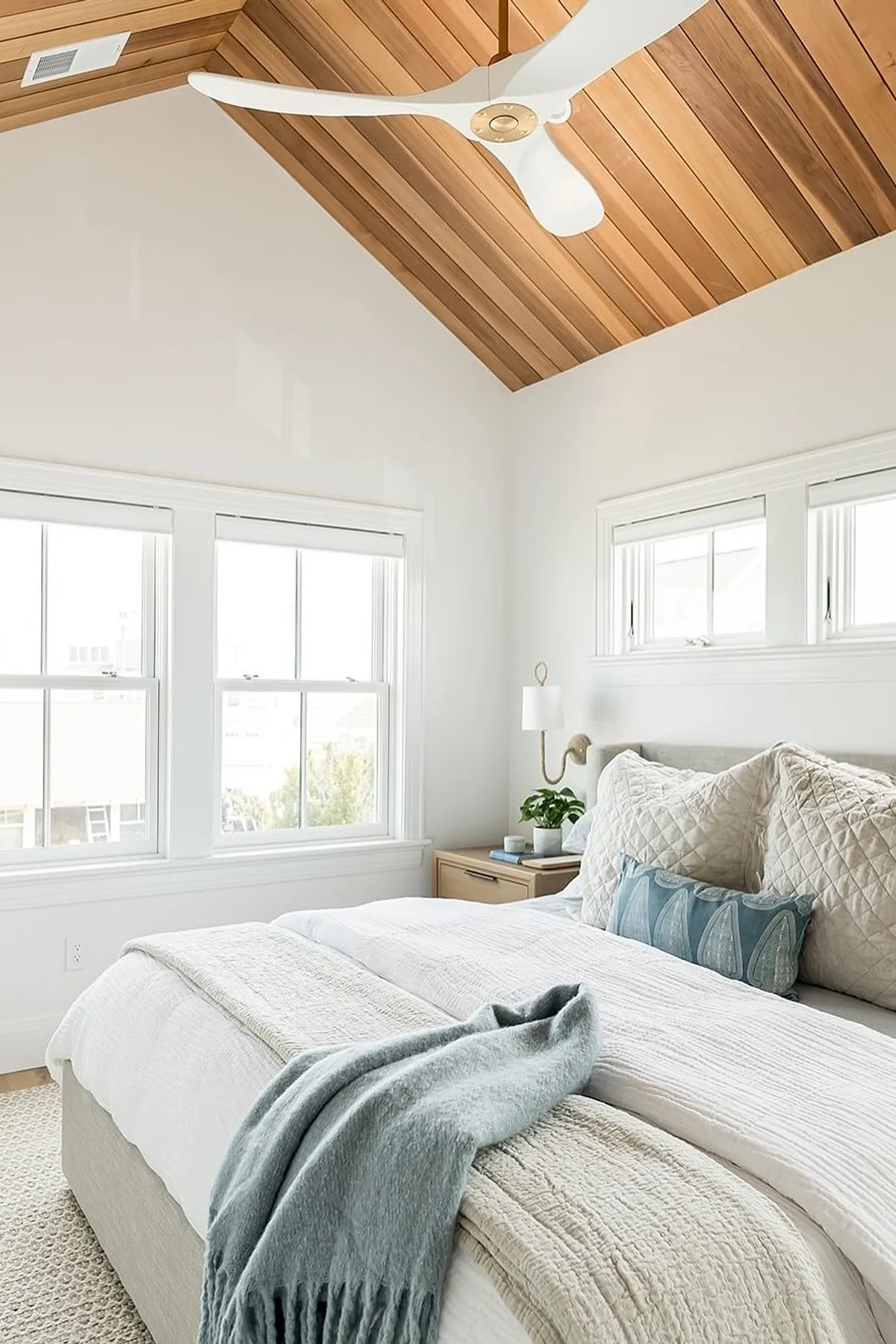 Bedroom with white bedding, light blue throw blanket, decorative blue pillow, and wood ceiling.