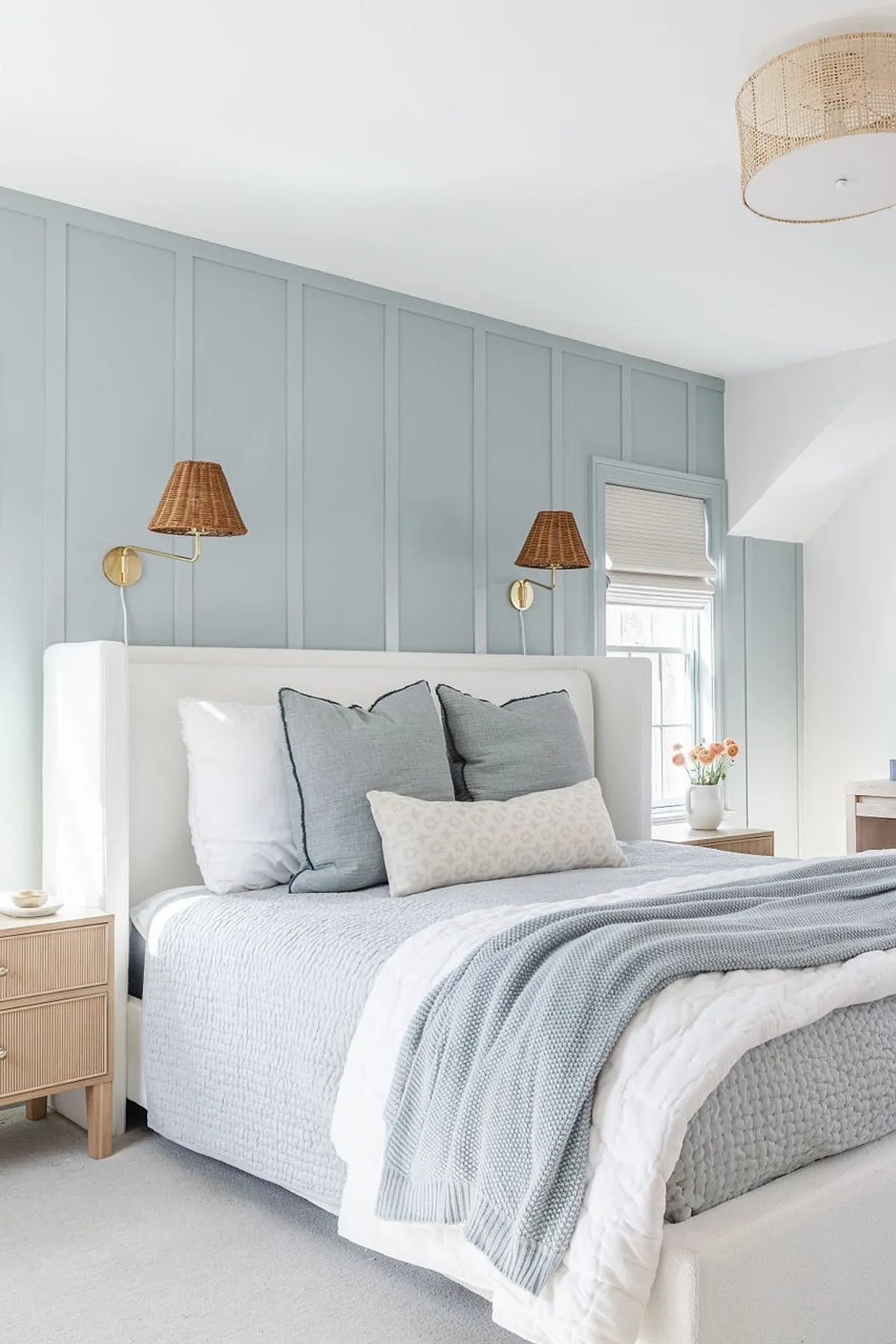 Bedroom with soft blue paneled wall, white bed, wicker lamps, and light wood side table.