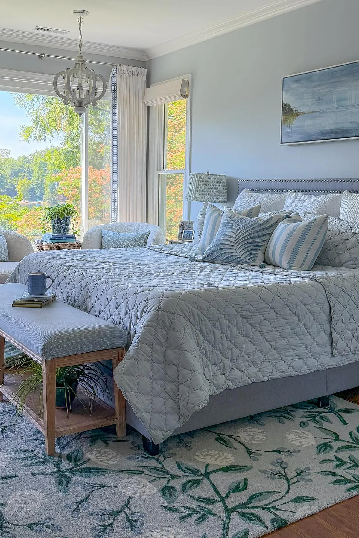 Bedroom with light blue quilted bedding, striped pillows, patterned rug, and large windows.