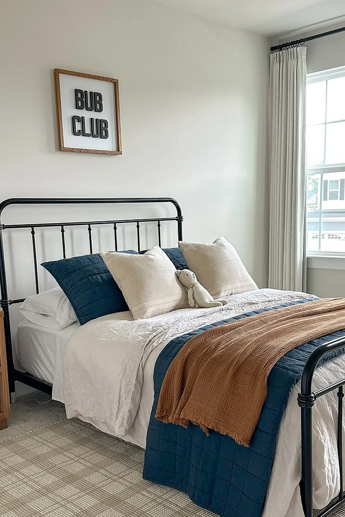 Bedroom with navy quilt, white bedding, iron bed frame, and framed wall art.