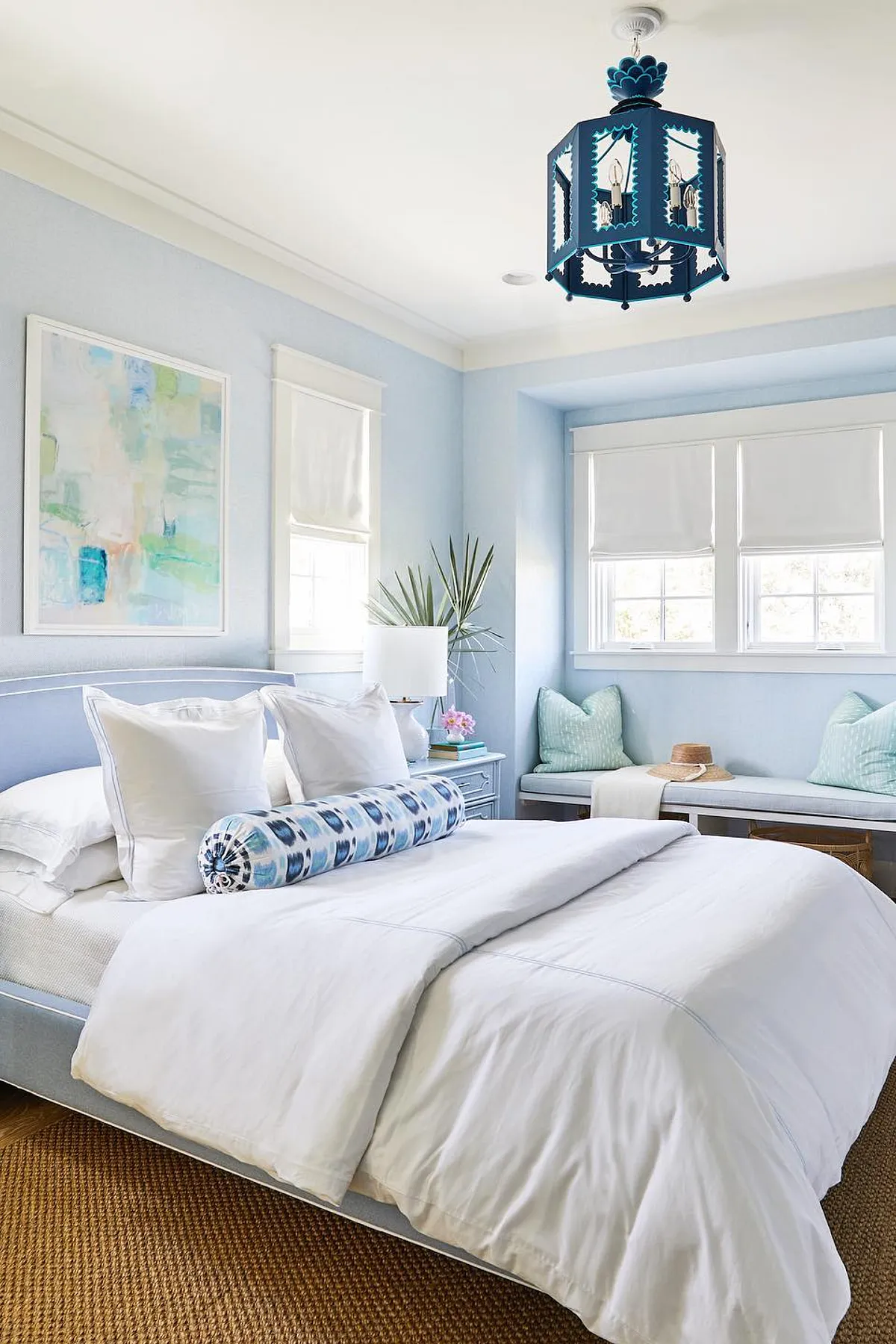 Bedroom with light blue walls, white bedding, decorative blue chandelier, and abstract art.