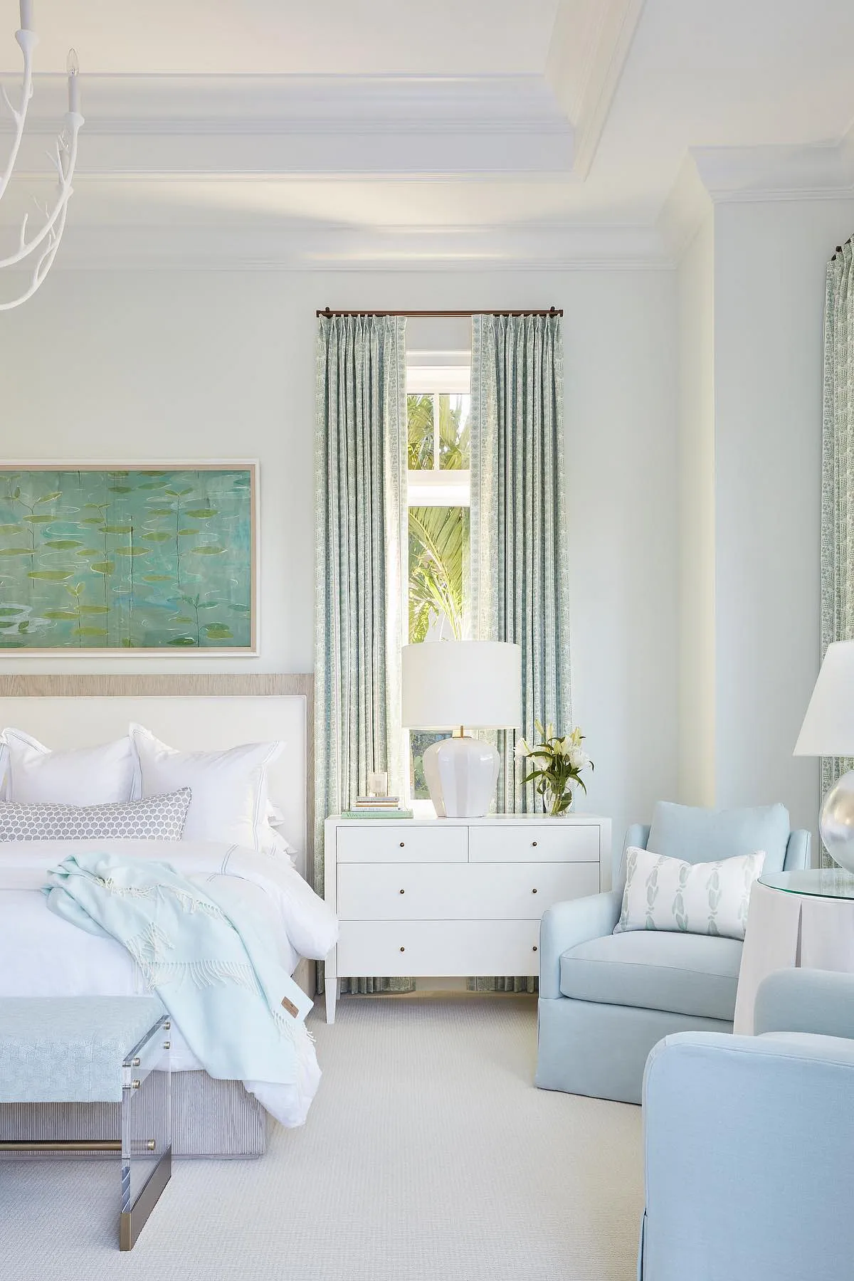 Bedroom with light blue curtains, white dresser, and matching chair against light walls.