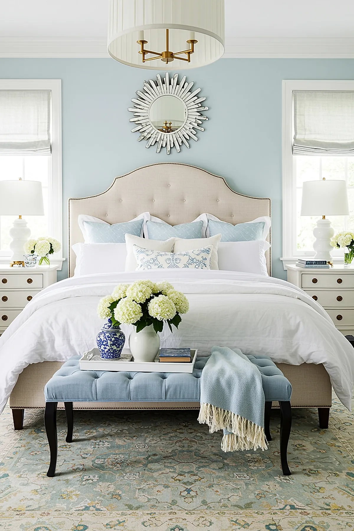 Bedroom with light blue accent wall, sunburst mirror, and blue upholstered bench.