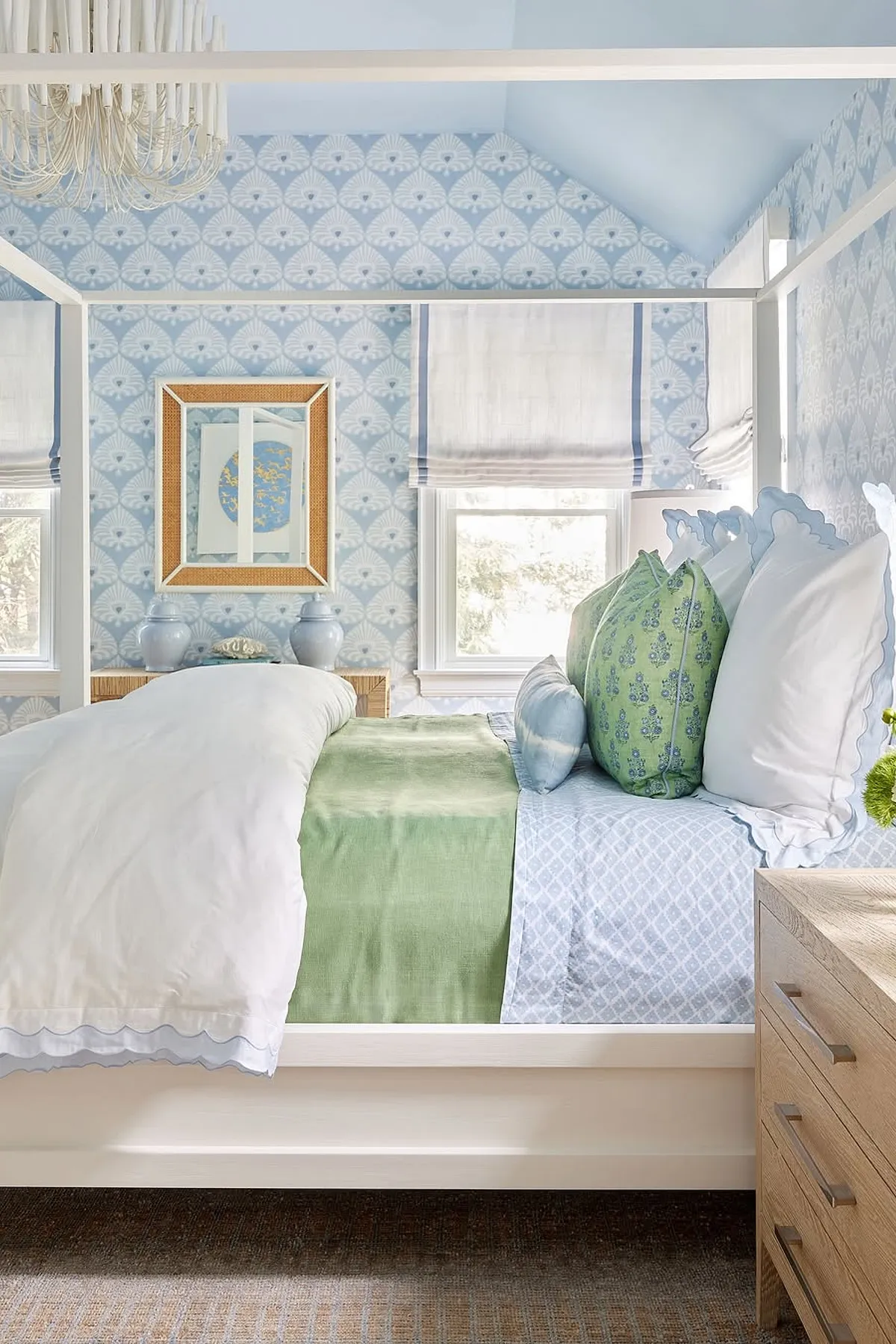 Bedroom with patterned blue wallpaper, white canopy bed, blue and green pillows, and chandelier.