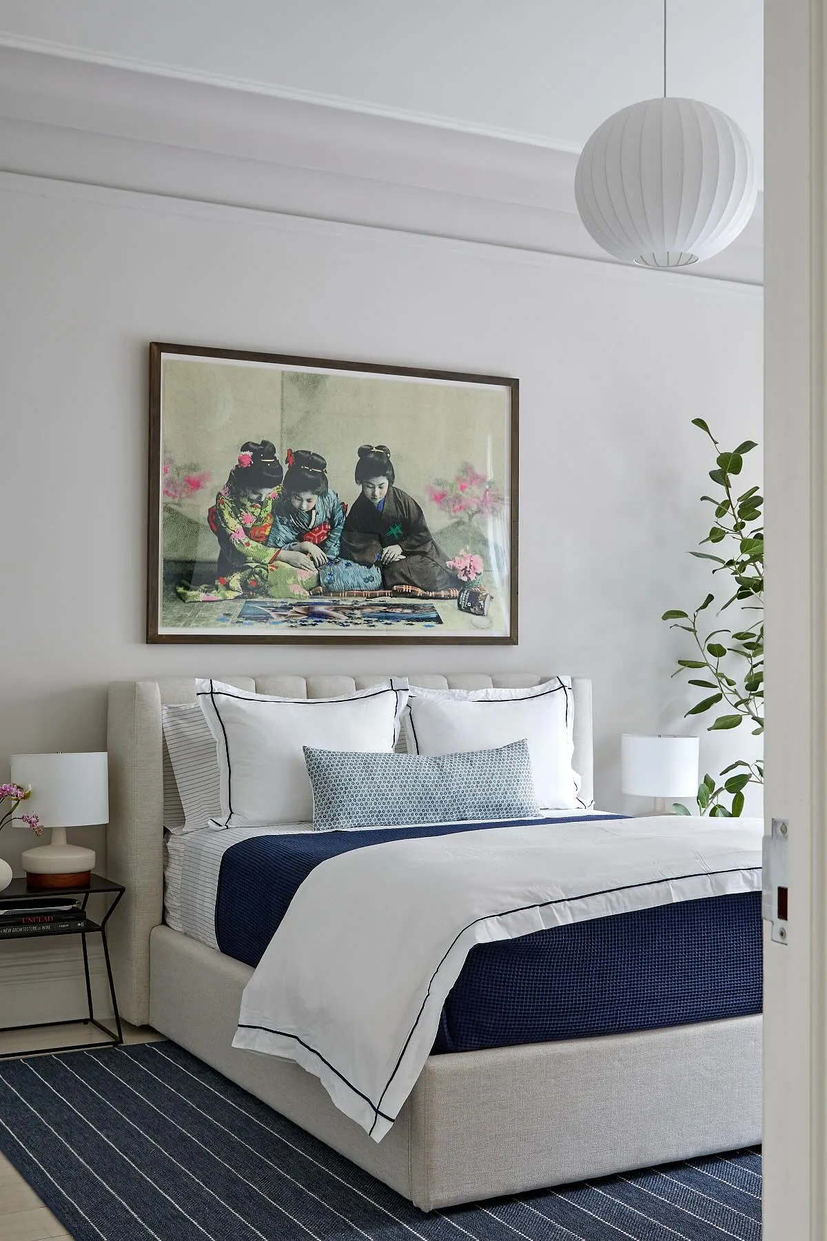 Bedroom with large artwork above bed, navy and white bedding, patterned pillow, and modern lighting.