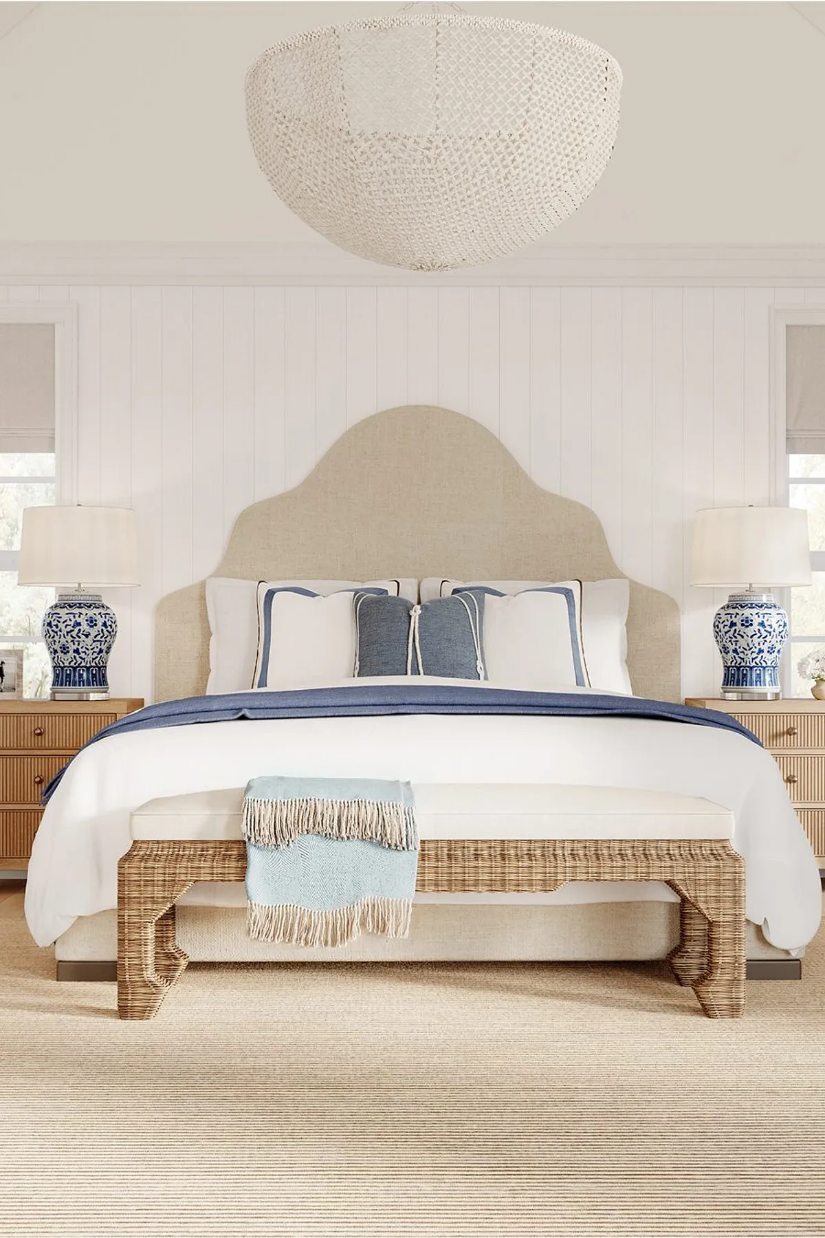 Bedroom with large woven chandelier, beige headboard, blue and white ceramic lamps, and white bedding.