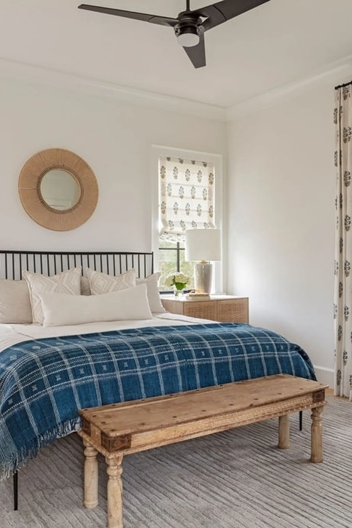 Bedroom featuring blue plaid throw on white bed, rustic wooden bench, wicker mirror, and ceiling fan.