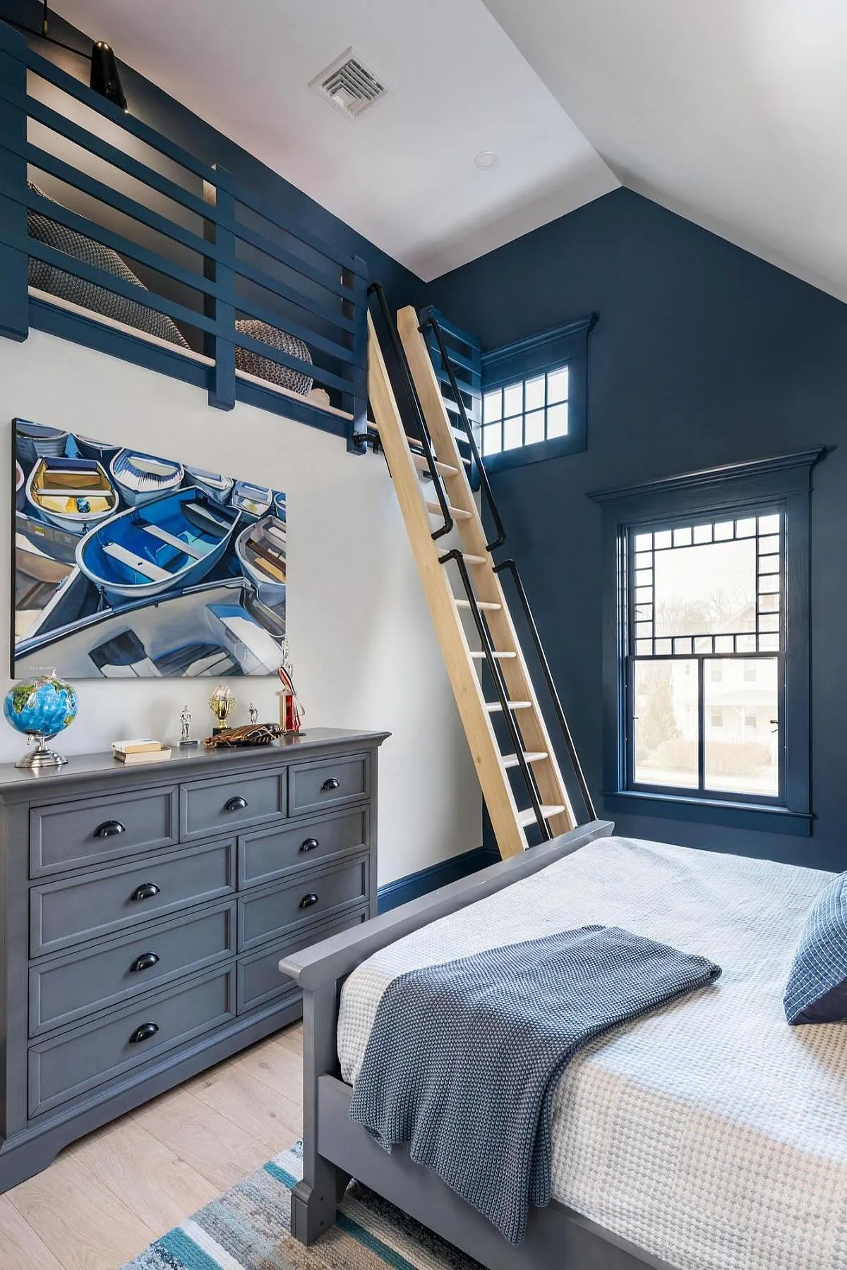 Navy blue bedroom with loft, wooden ladder, nautical artwork, and dresser.
