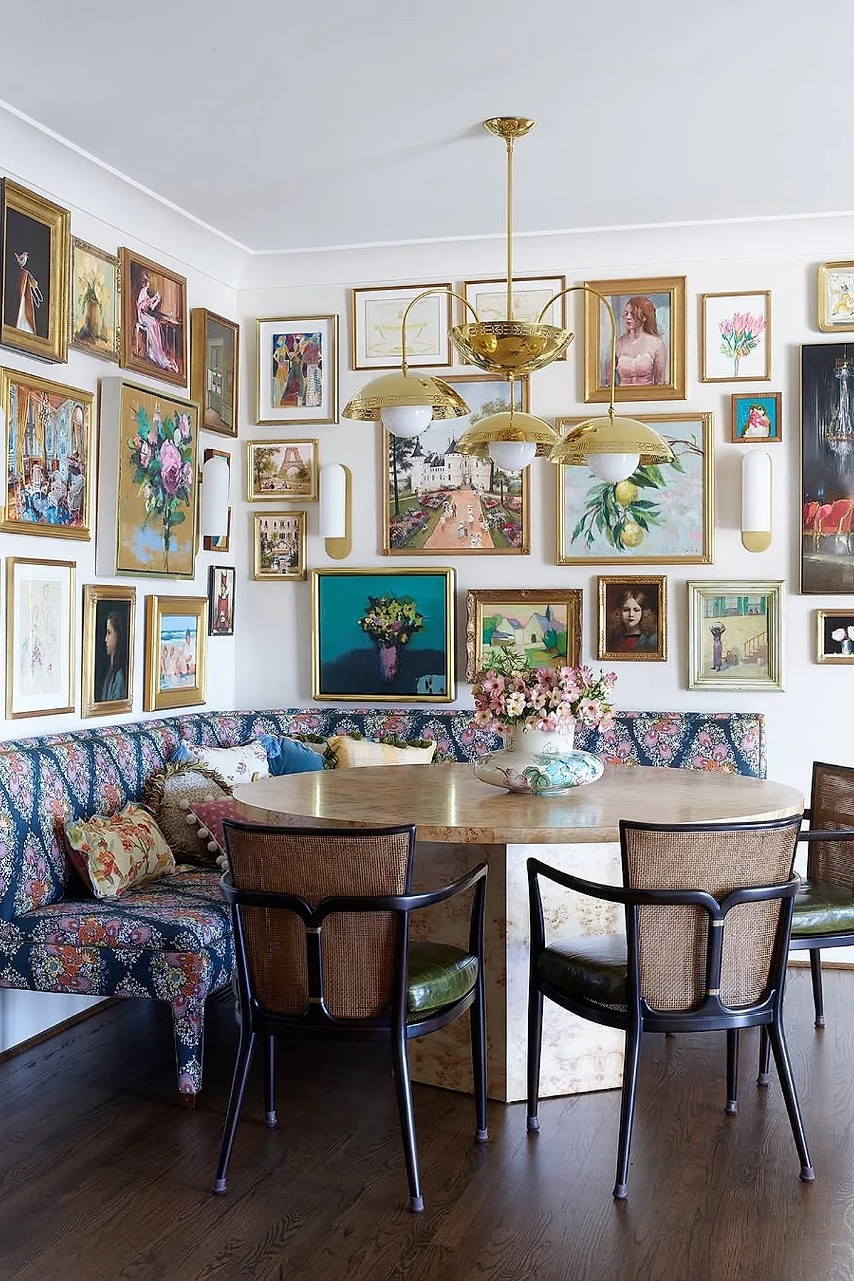 Dining area with a vibrant gallery wall featuring eclectic art pieces in gilded frames, floral upholstery, and plush seating.