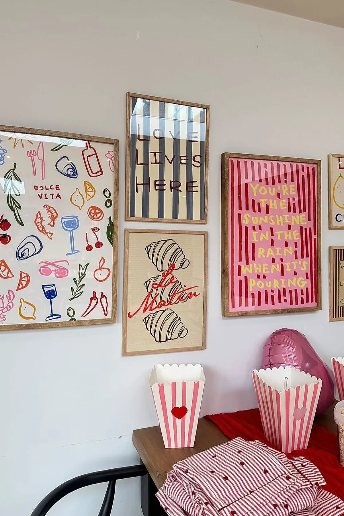 Gallery wall with playful typography and vibrant illustrations in a dining nook, featuring bold colors and striped patterns.