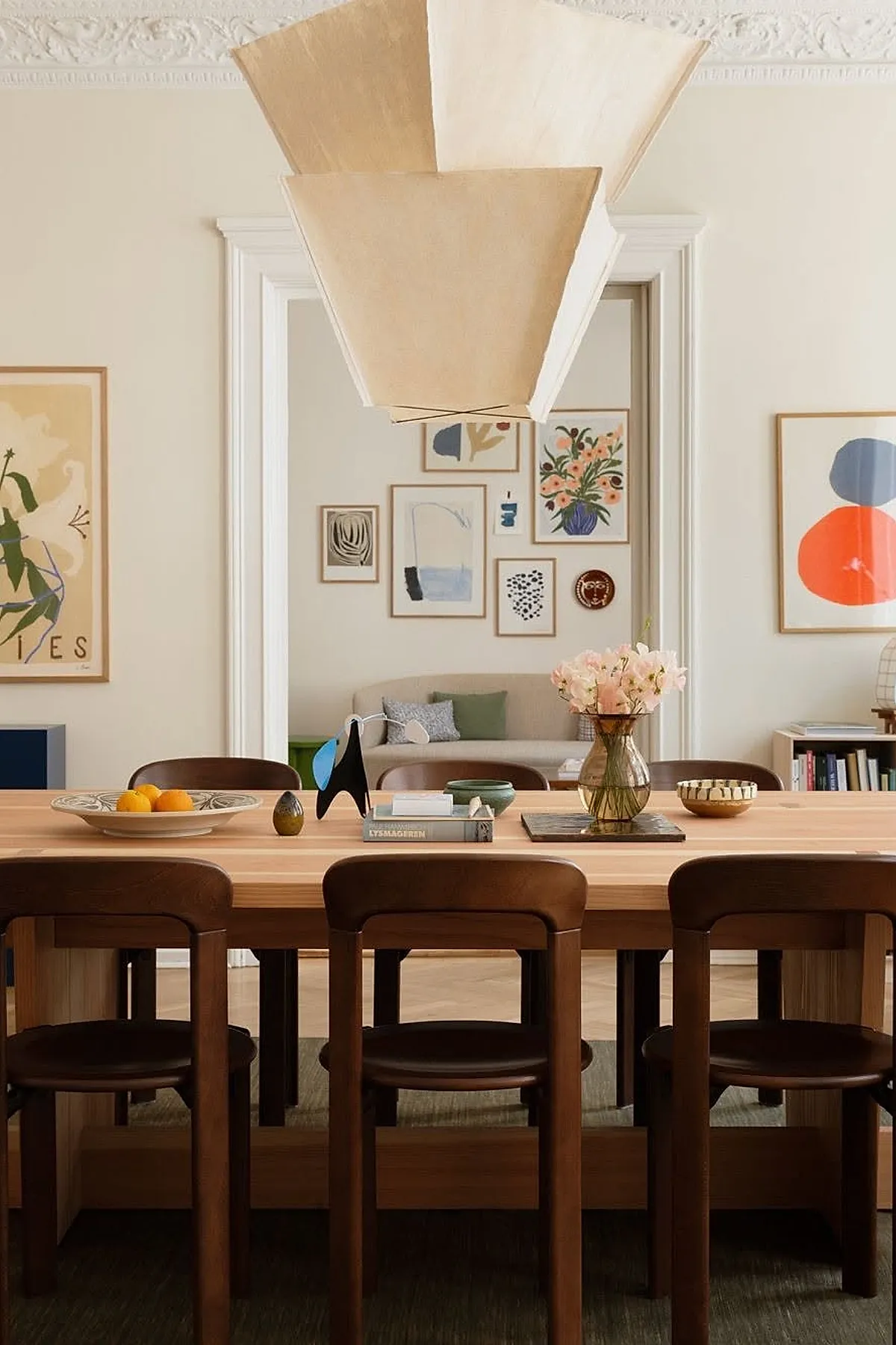 Dining room with a modern gallery wall featuring abstract art in minimalist frames, complemented by wooden furniture and a large pendant light.