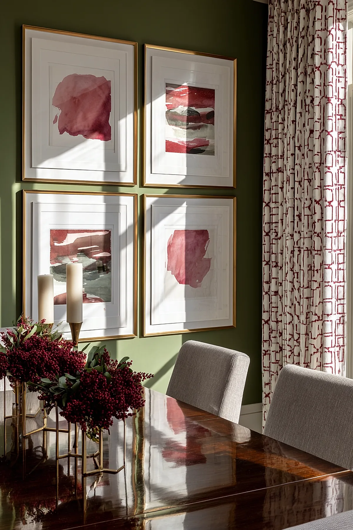 Green wall with framed red art and patterned curtains in dining area.