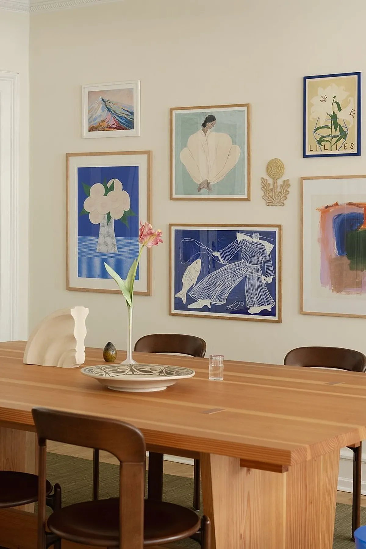 Dining room with a modern gallery wall featuring colorful abstract art in wooden frames, paired with a wooden table and chairs.