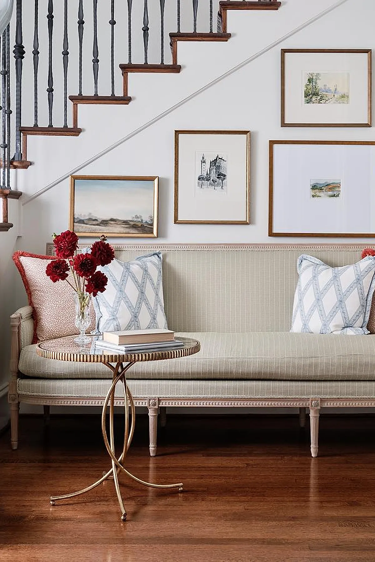 Living room with classic gallery wall featuring framed artwork in gold frames, a neutral sofa, and decorative pillows near a staircase.