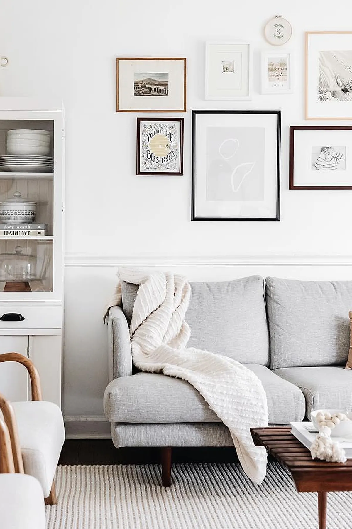 Living room with a neutral gallery wall featuring diverse framed art pieces above a gray sofa with a textured throw.