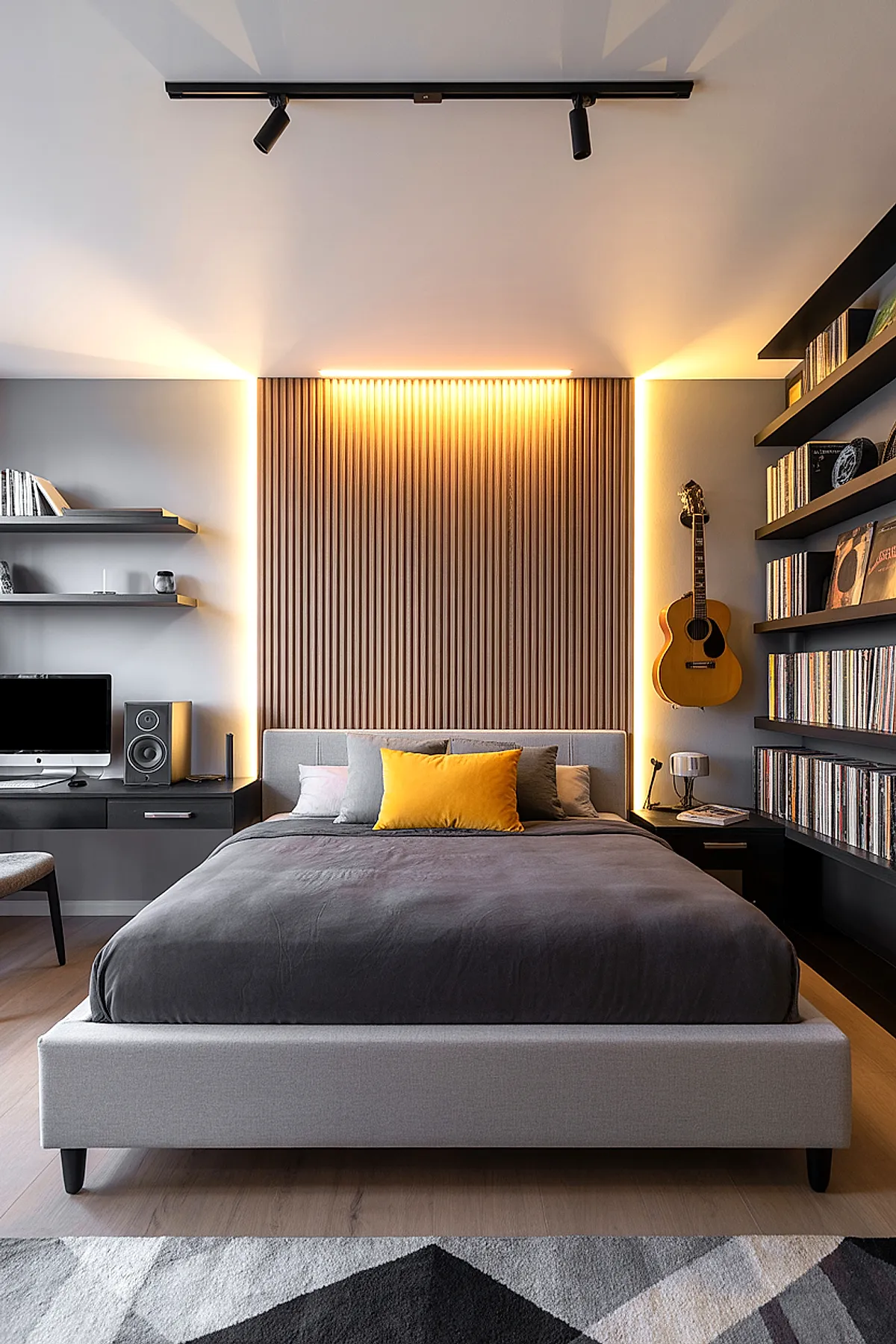 Modern teen boy bedroom featuring a bed with gray upholstered frame, dark gray bedding, multiple pillows including a bright yellow one, vertical wooden slat accent wall behind the bed with warm backlighting, black floating shelves holding books and records on either side, an acoustic guitar hanging on the right wall.