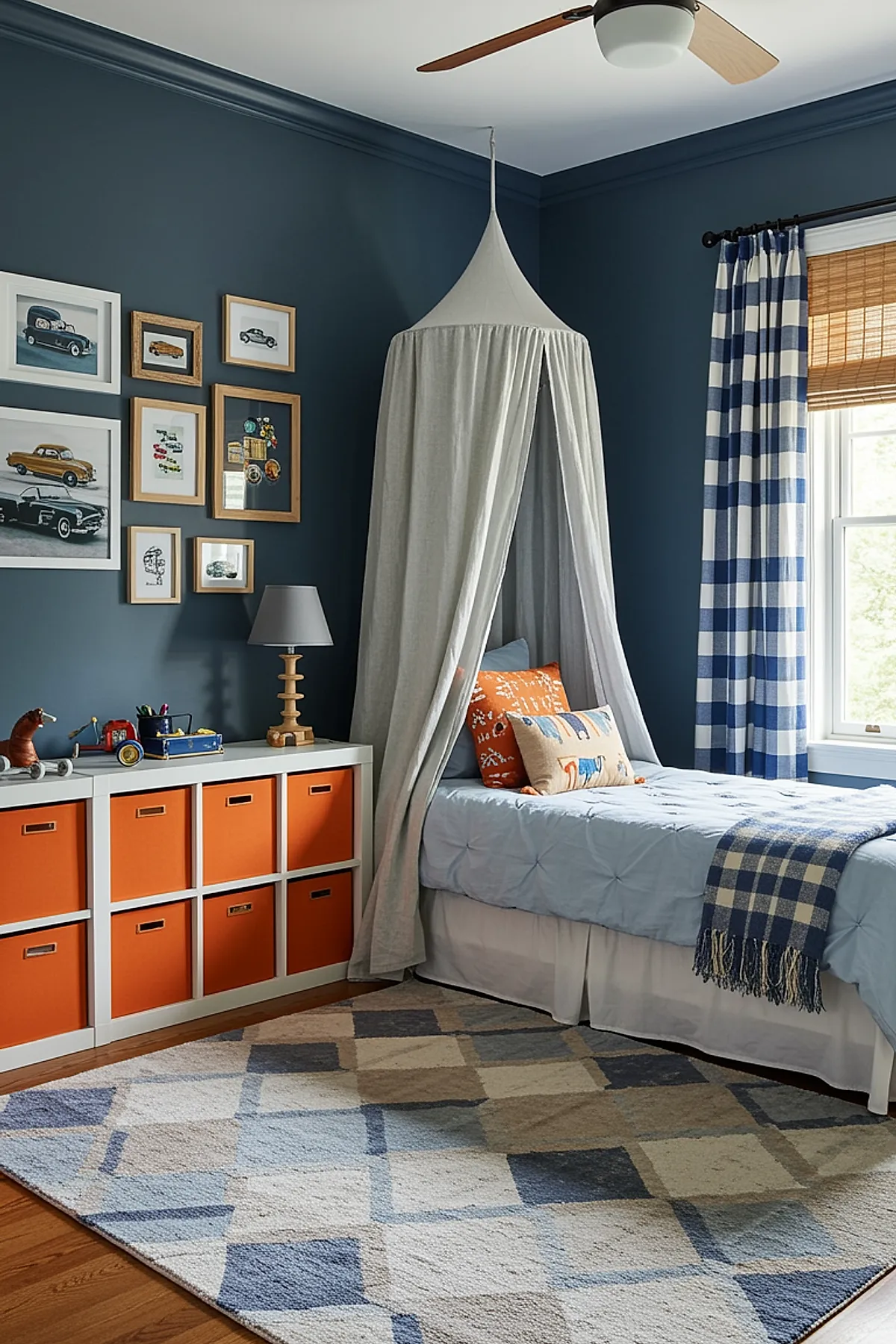 Boys bedroom featuring dark blue walls, white canopy bed with light blue bedding and patterned pillows, white storage unit with bright orange fabric bins, framed vintage car prints on wall, blue and white checkered curtains, woven window blind.