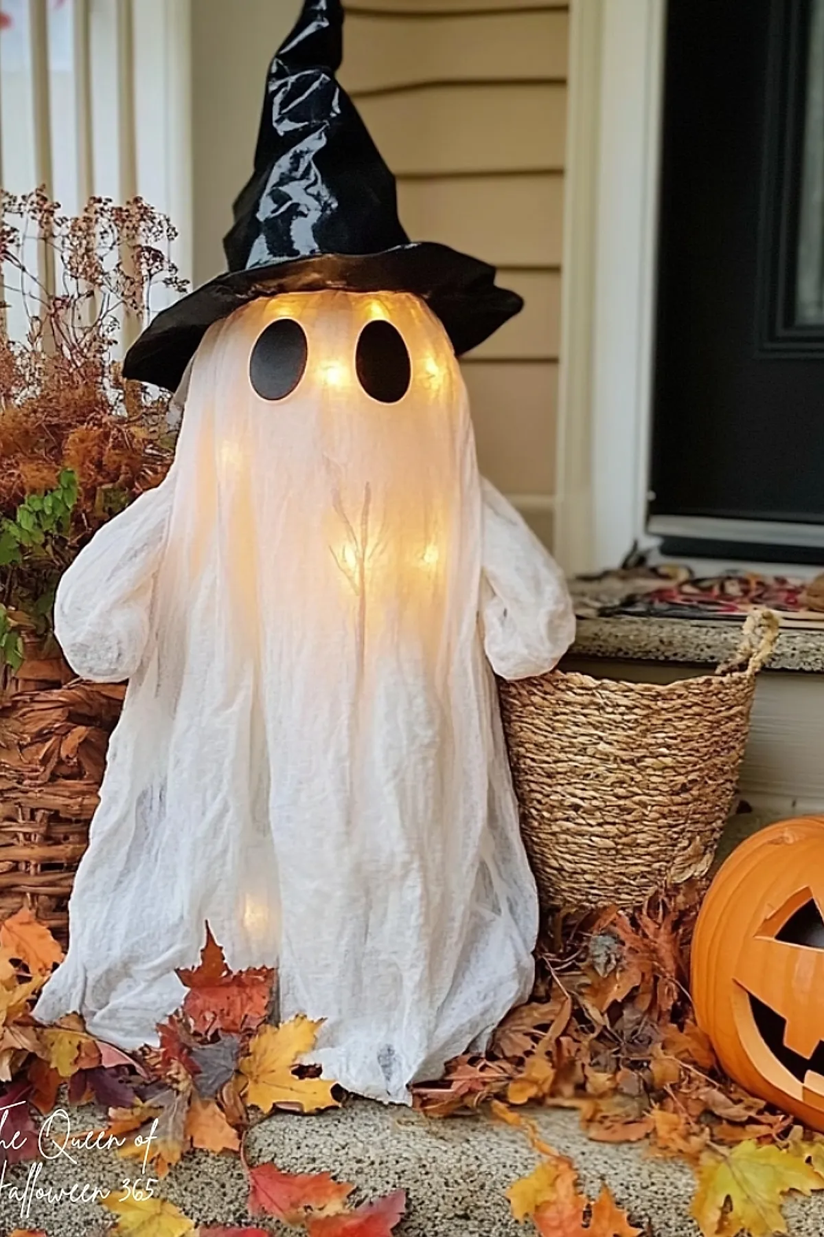 white glowing ghost figure wearing black shiny witch hat surrounded by dried leaves orange pumpkin woven basket and porch steps