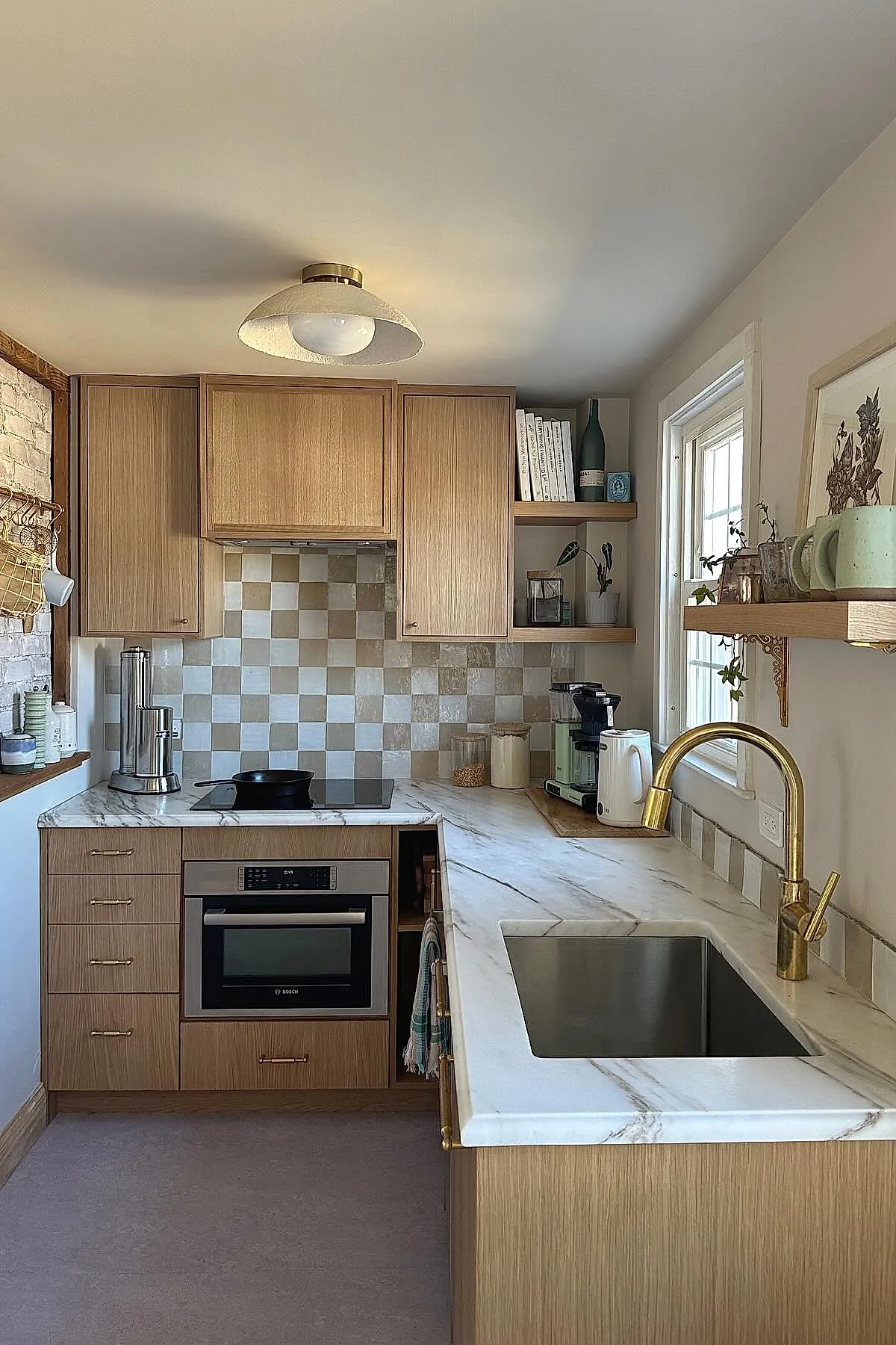 small L-shaped kitchen with marble countertops, light wood cabinets, brass faucet, checkered tile backsplash, open wooden shelves near window