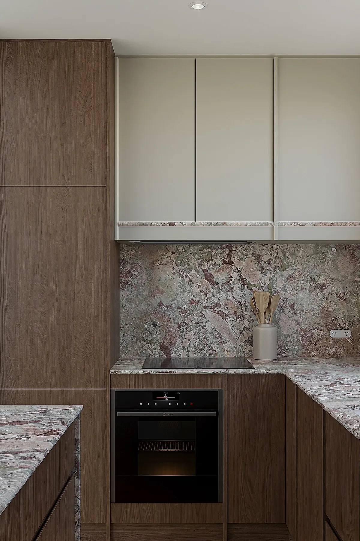 small kitchen with dark wood lower cabinets, beige upper cabinets, matching marble countertops and backsplash in pink and gray tones, built-in black oven, ceramic utensil holder