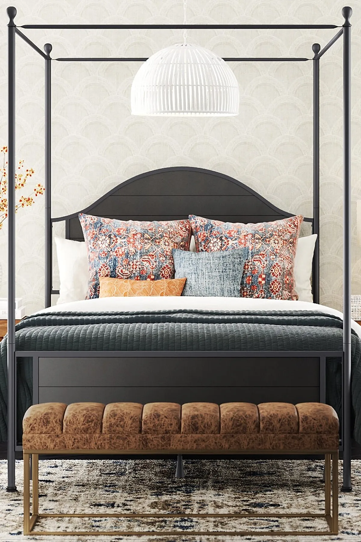 Black metal canopy bed with arched headboard, bedding with red and blue patterned pillows, gray quilted blanket, brown tufted leather bench with gold legs at foot of bed, light textured area rug.