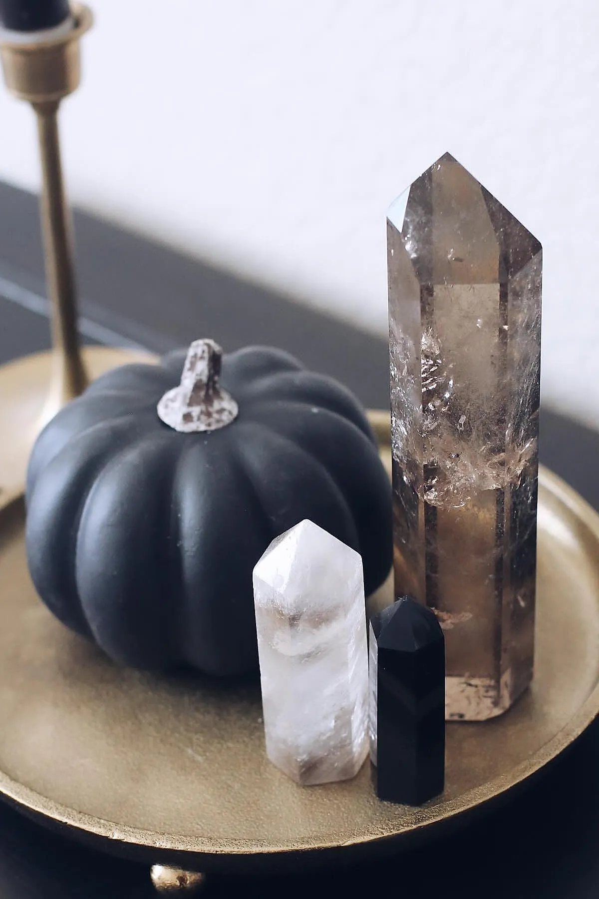 Matte black pumpkin paired with three polished crystal towers in white, black, and smoky brown colors arranged on a round gold metal tray.
