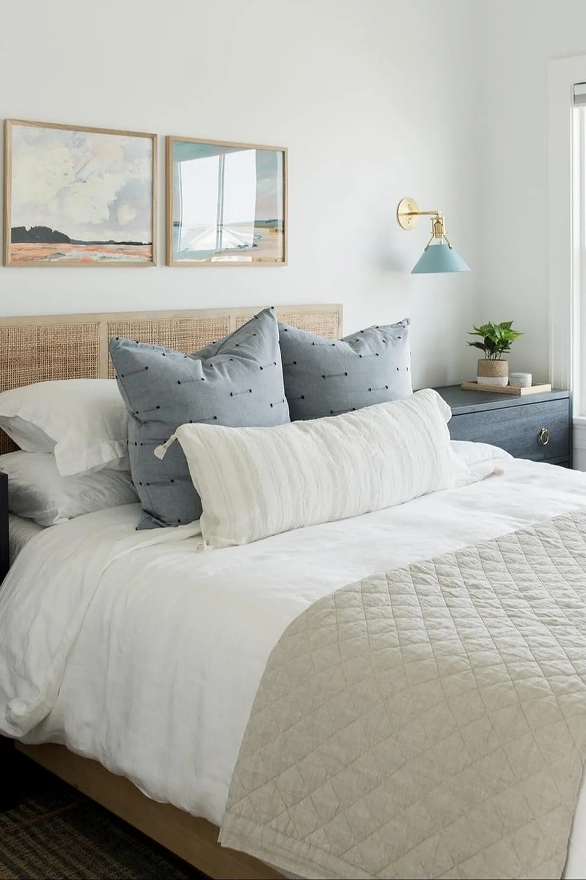 Bedroom with blue pillows, white bedding, rattan headboard, and blue wall sconce.