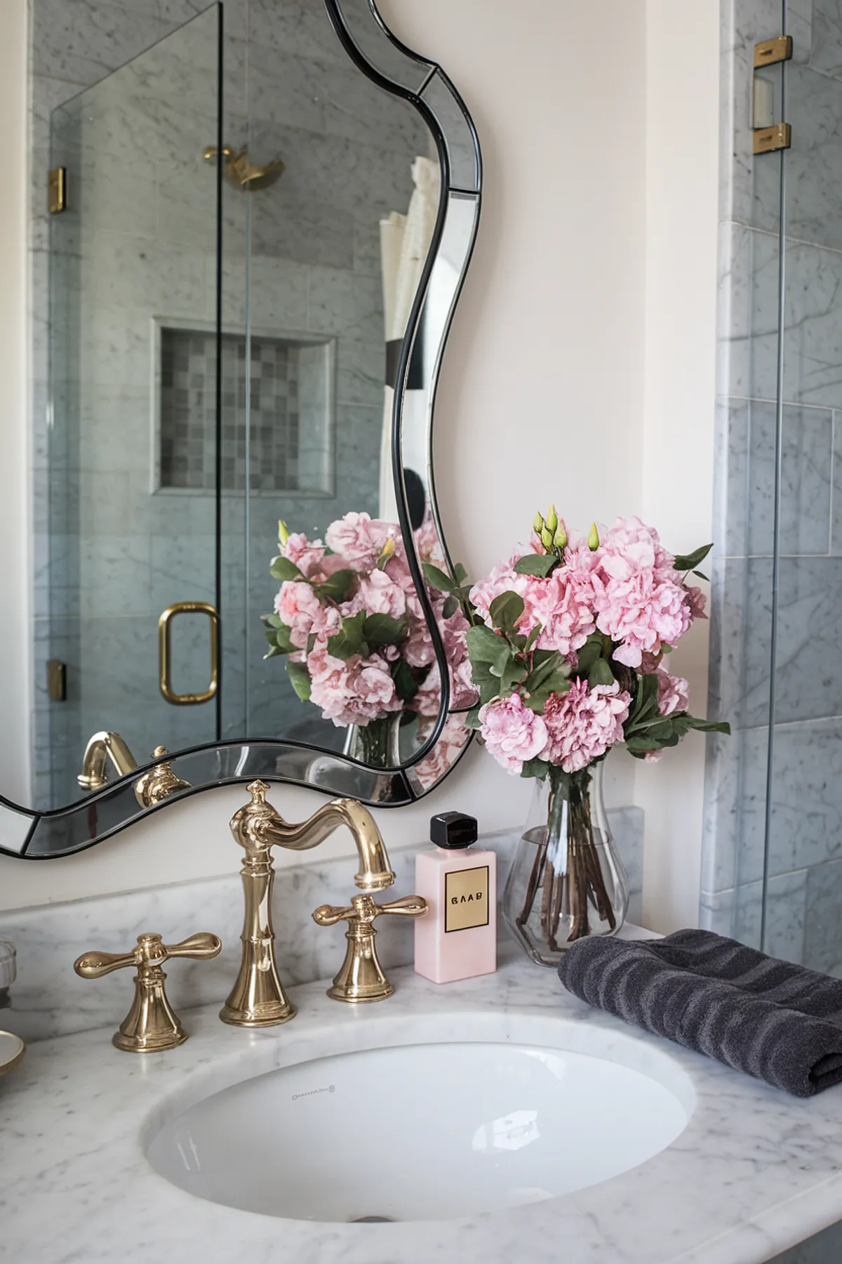 A stylish bathroom with pink flowers, gold fixtures, and an elegant mirror.