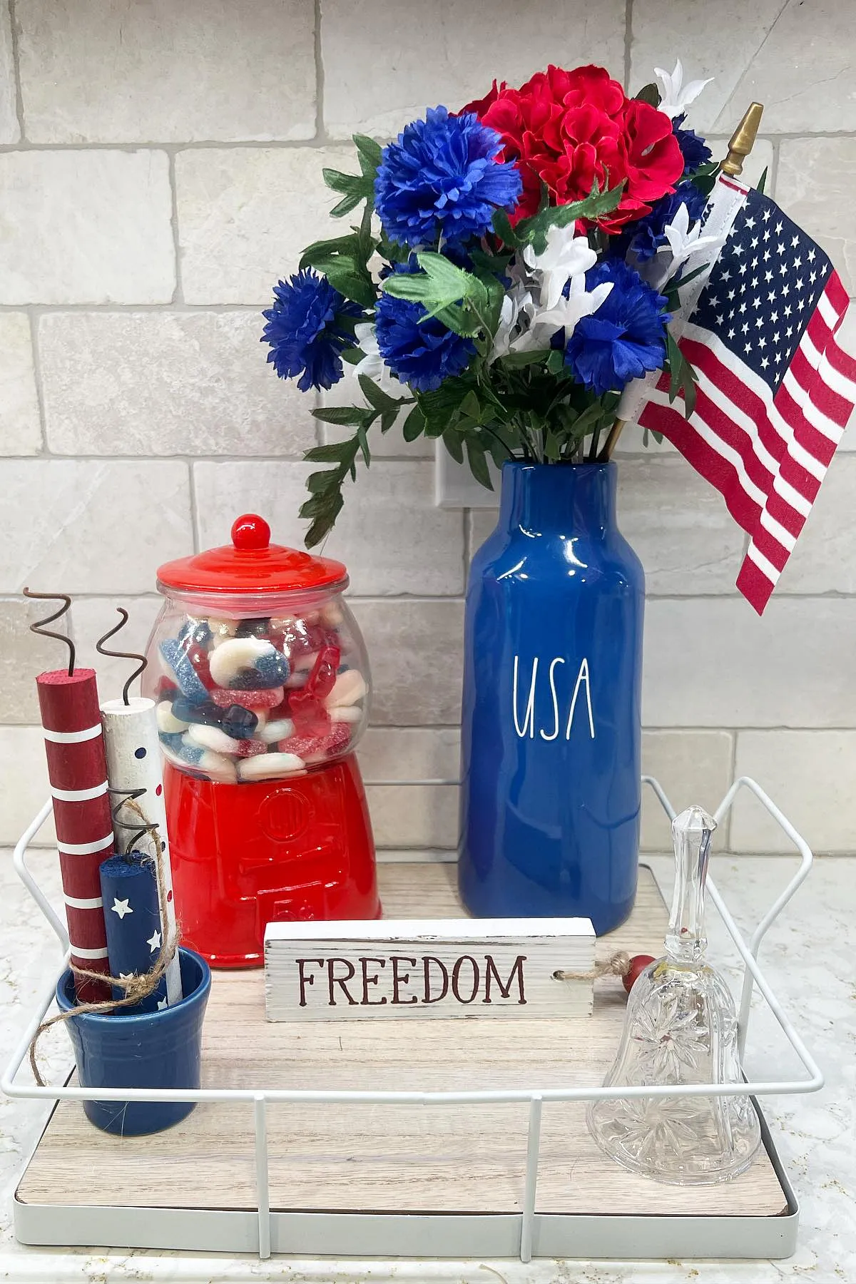 A 4th of July themed decor with a blue vase of flowers, red gumball machine, and a 'Freedom' sign.